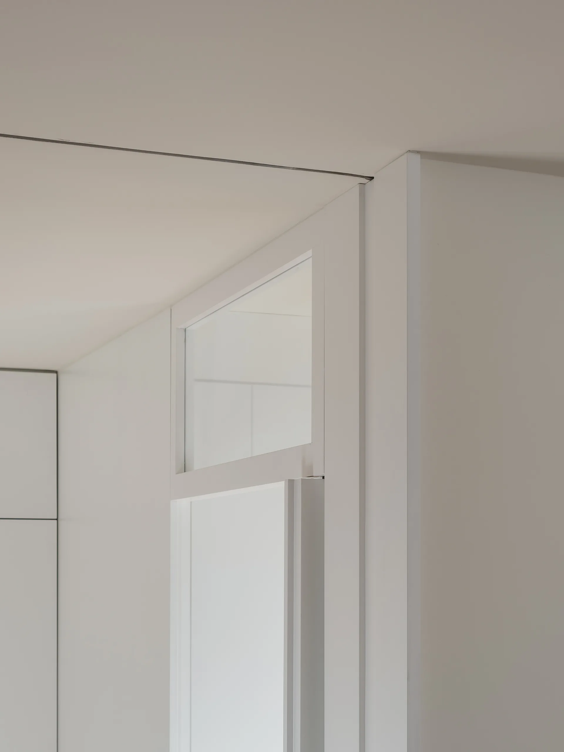 Close-up of a minimalist white door frame featuring a clear glass transom window set against a clean matte white wall and ceiling.