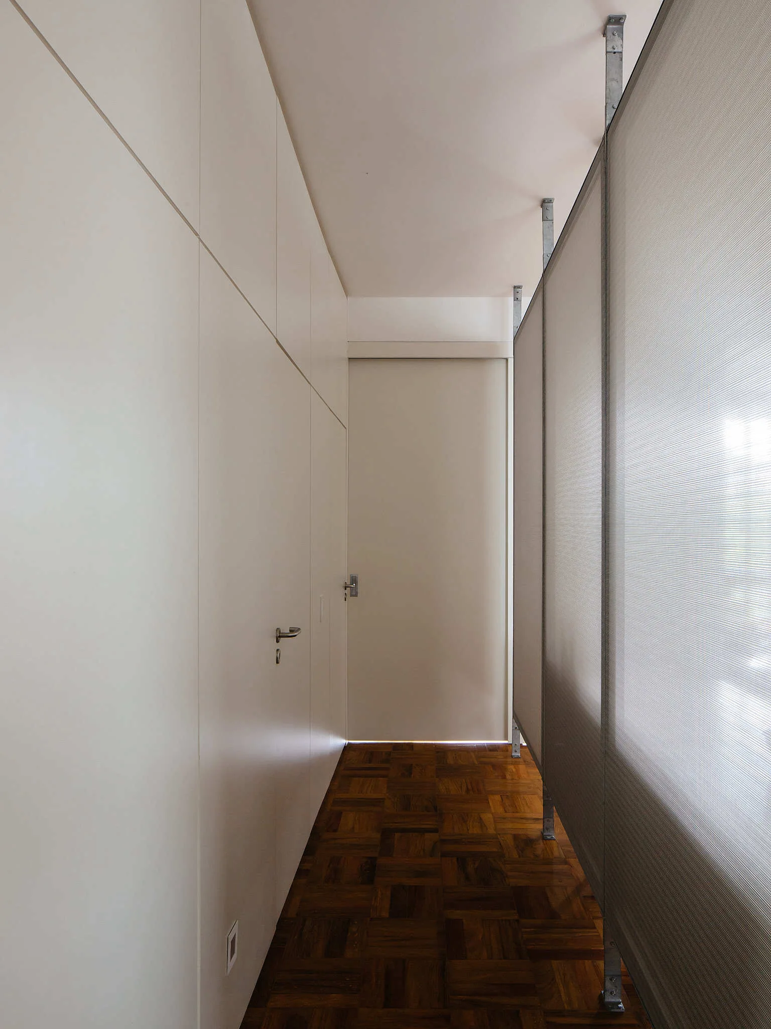 A minimalist hallway features off-white built-in cabinetry, a translucent room divider screen, and dark wood parquet floors.