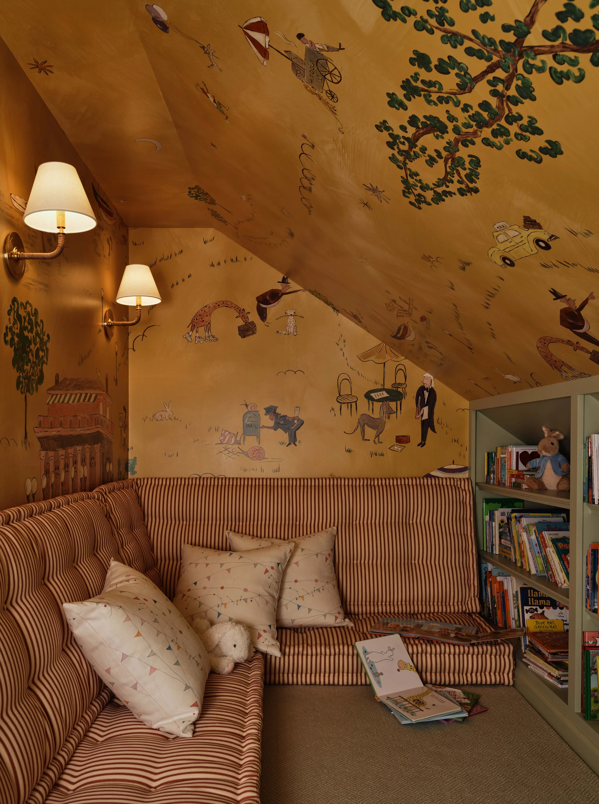 A cozy kids reading nook under a sloped ceiling features a striped red bench, a sage green bookshelf, and ochre walls with whimsical illustrations.