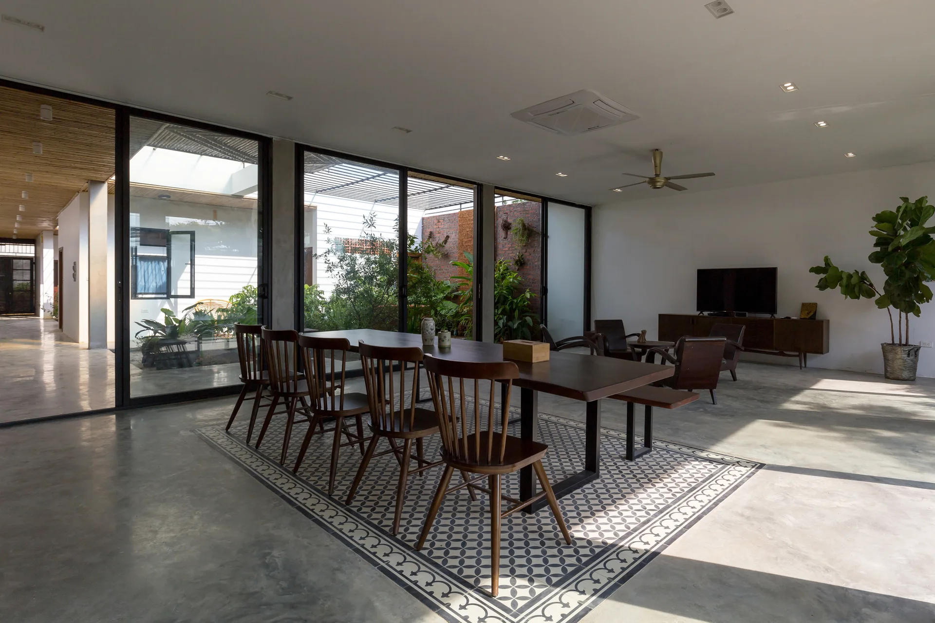 A wooden dining table with spindle-back chairs rests on a patterned tile inlay within a polished concrete floor next to glass doors.