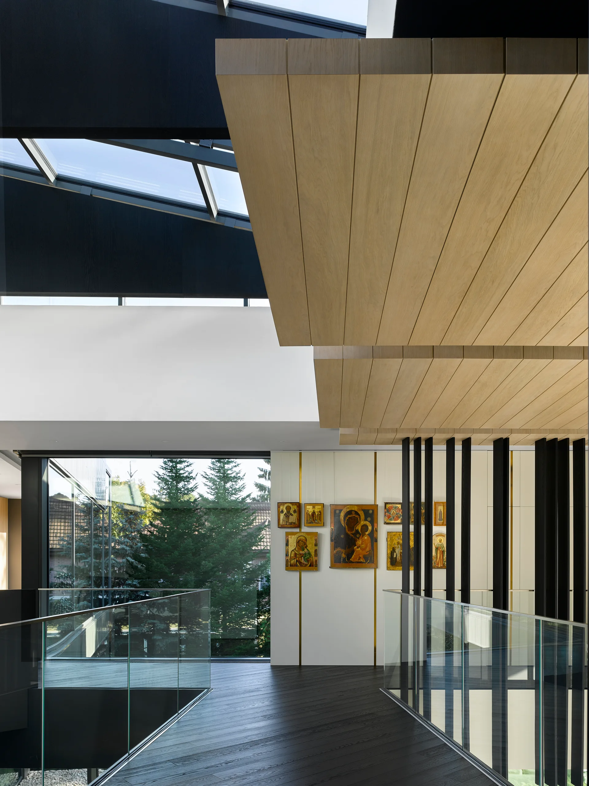 A modern interior landing features a light oak planked ceiling, black vertical slat partitions, glass railings, and wall-mounted art icons.