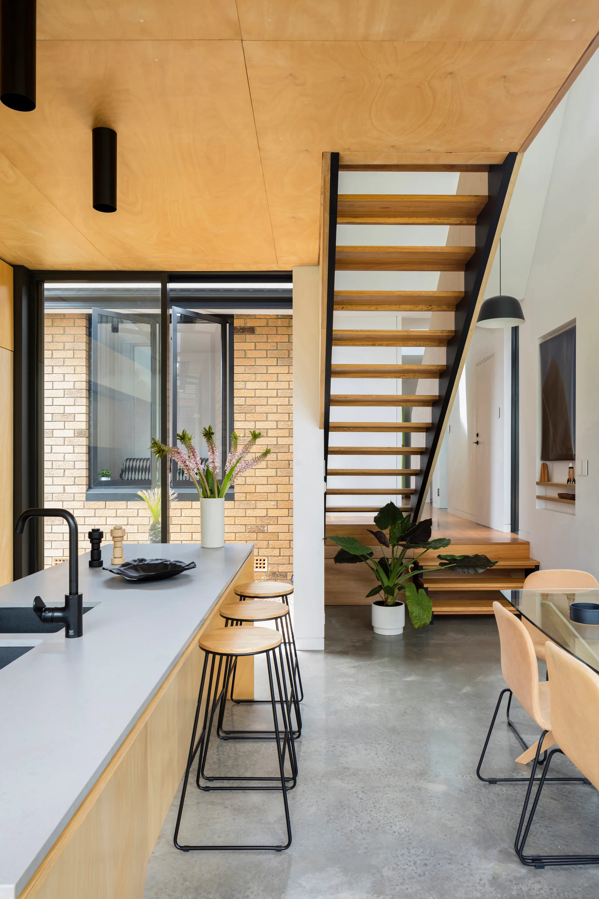 A modern kitchen featuring a wood panel ceiling, concrete floor, light gray island with barstools, and an open riser staircase.