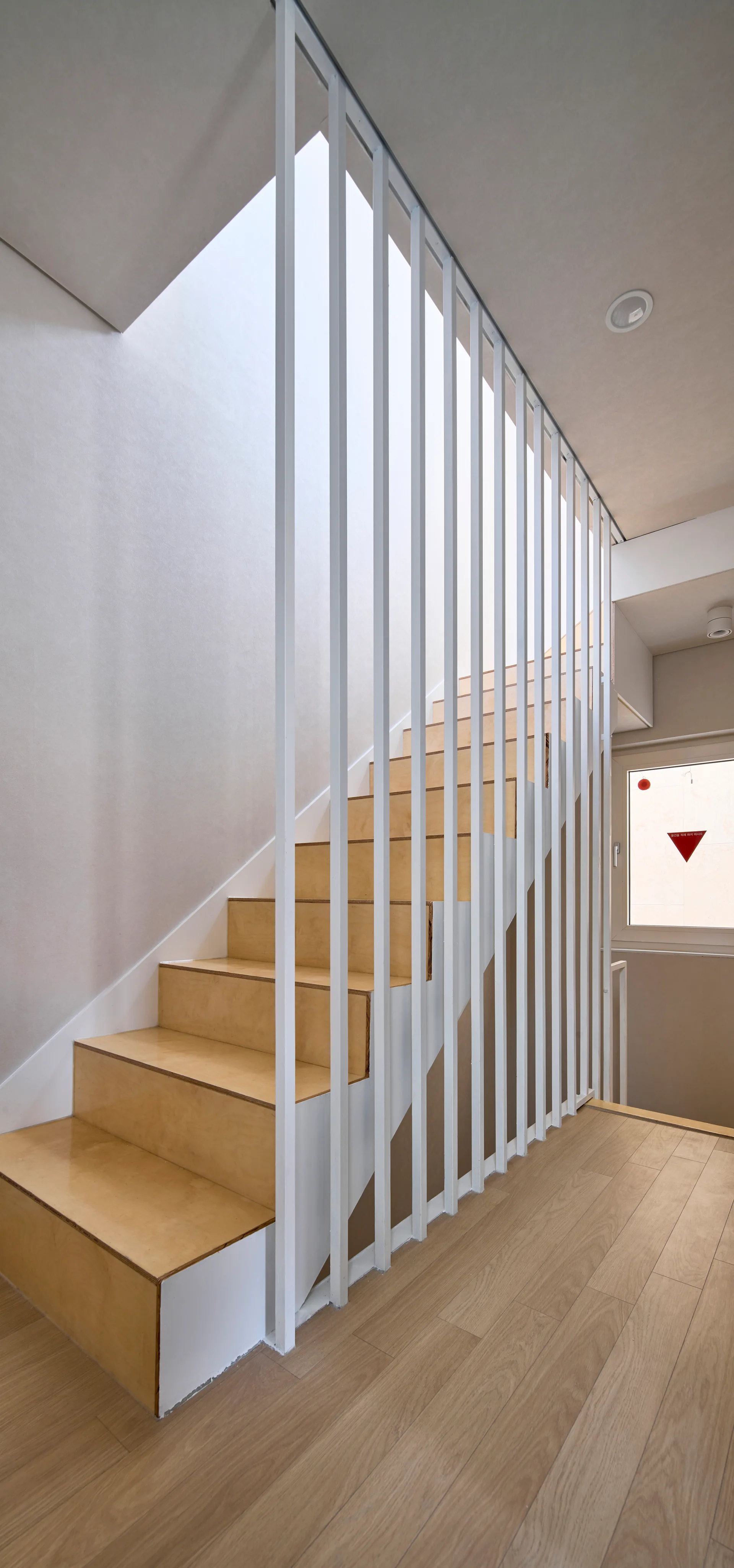 A minimalist staircase featuring light wood treads and a white metal vertical baluster screen against plain white walls.