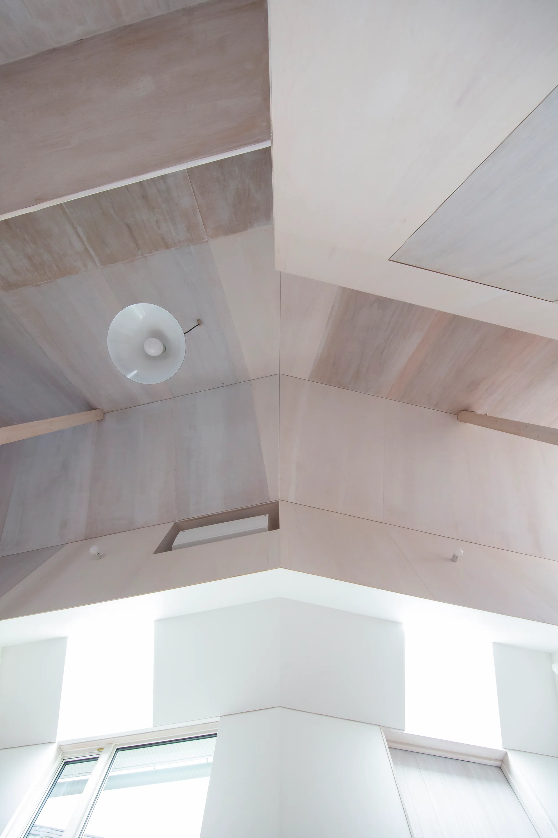 An upward view of a vaulted ceiling lined with light-toned wood panels and a central white dome pendant light.
