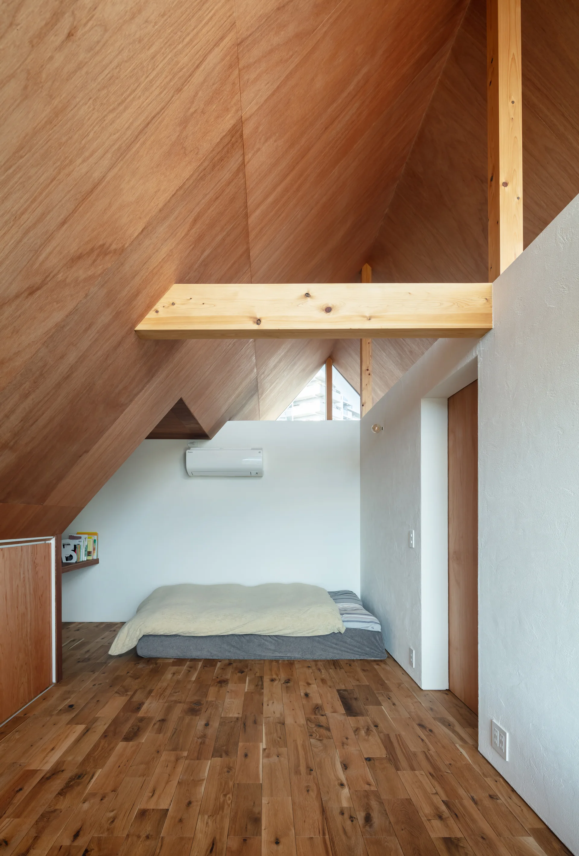 A minimalist attic bedroom featuring a low-profile bed beneath a steeply sloped wood-paneled ceiling with an exposed timber beam.