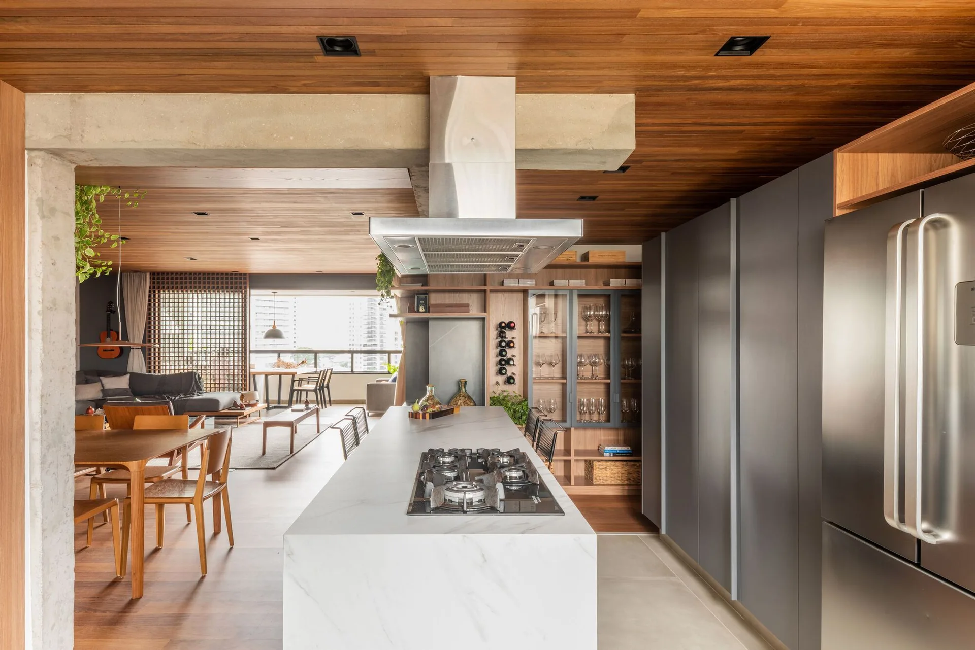 An open-concept kitchen features a white marble island with a gas stove, surrounded by matte gray cabinets and a rich wood-plank ceiling.