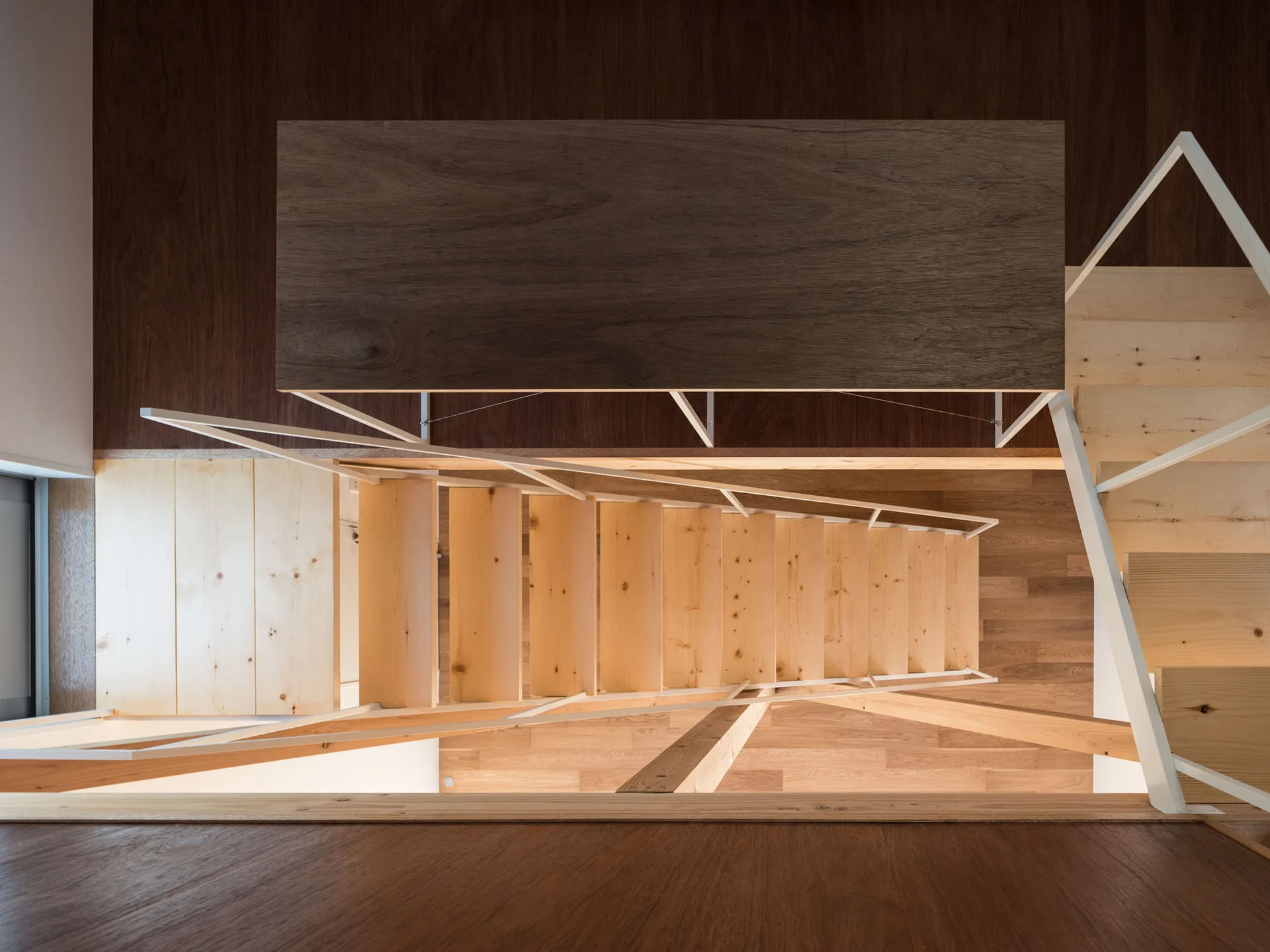 An overhead view looking down a light wood staircase featuring a geometric white metal handrail and contrasting dark wood flooring.