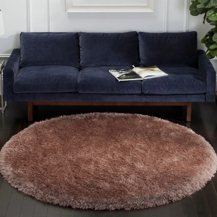 A navy blue fabric sofa stands on a dark wood floor in front of a white wall, paired with a large round shaggy brown rug.