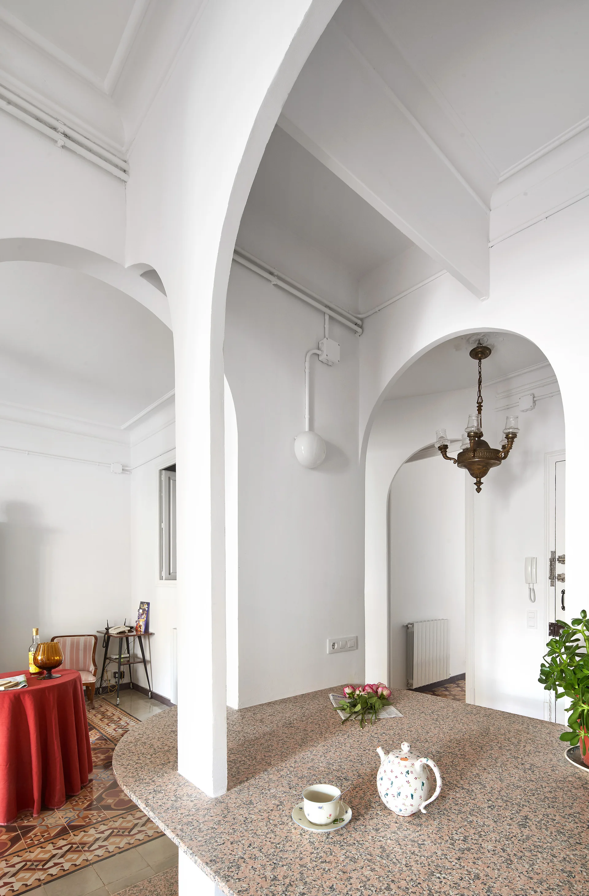 White arched doorways frame a view from a speckled stone kitchen island with a tea set to a dining area with patterned tile floors.