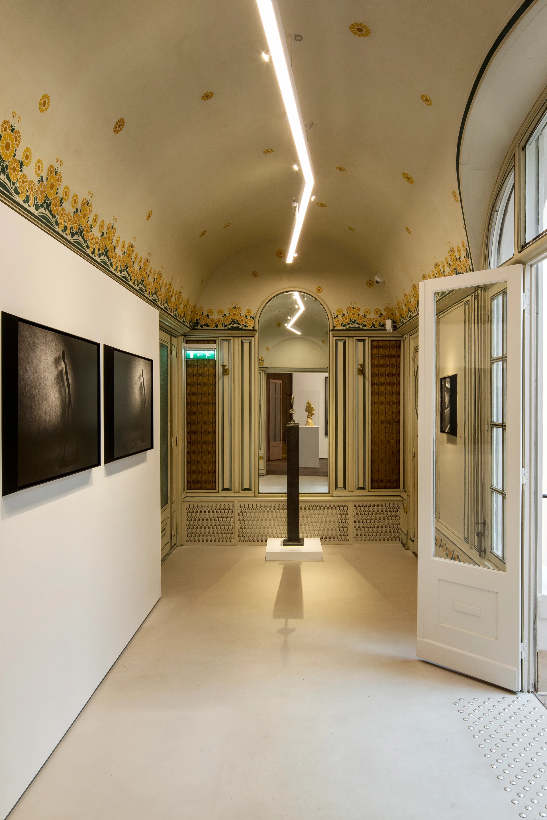 A long gallery hallway features an off-white vaulted ceiling with yellow flower stencils, a modern track light, and a white french door.