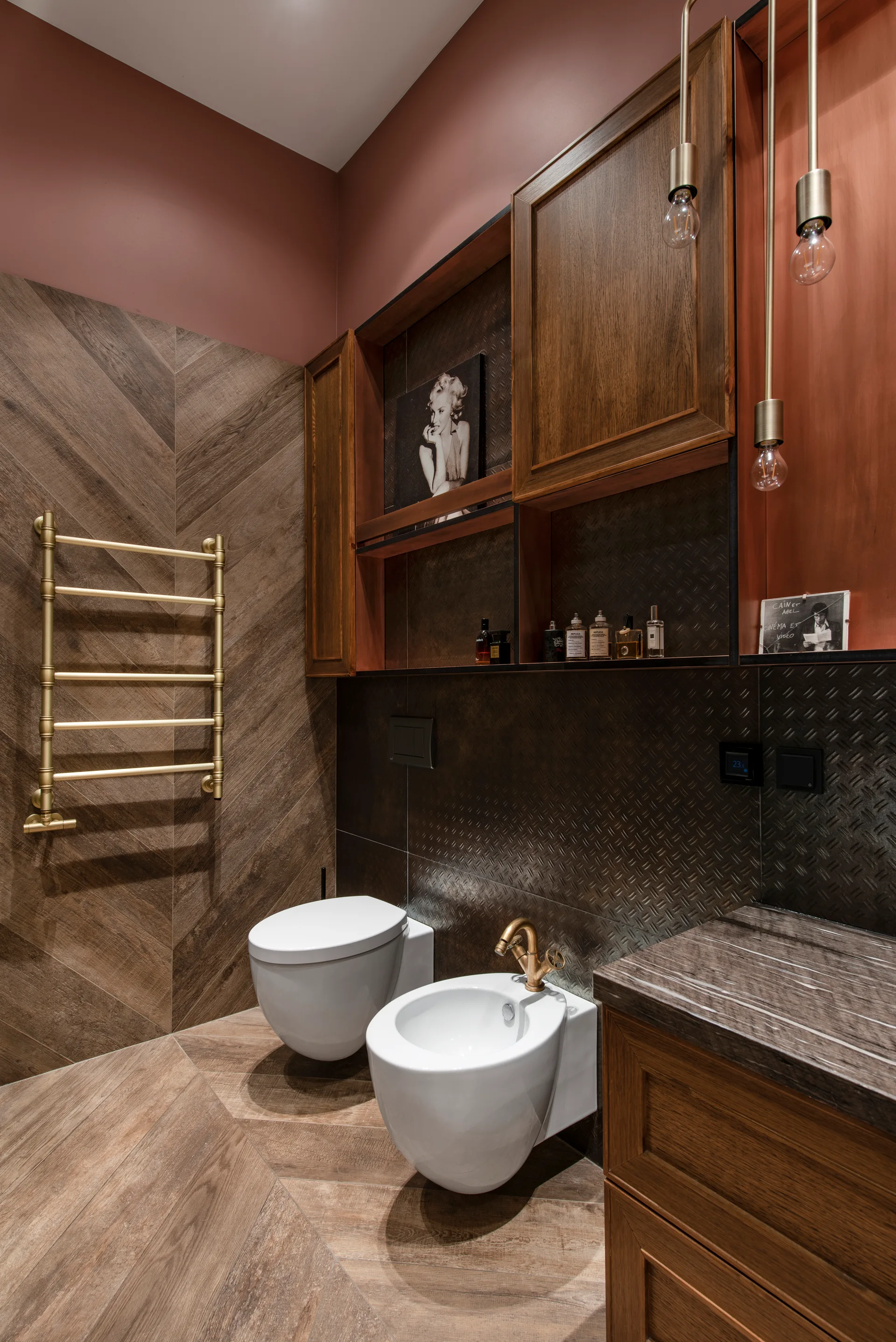 A modern bathroom featuring a wall-mounted toilet and bidet, chevron wood wall paneling, and a brass towel warmer.