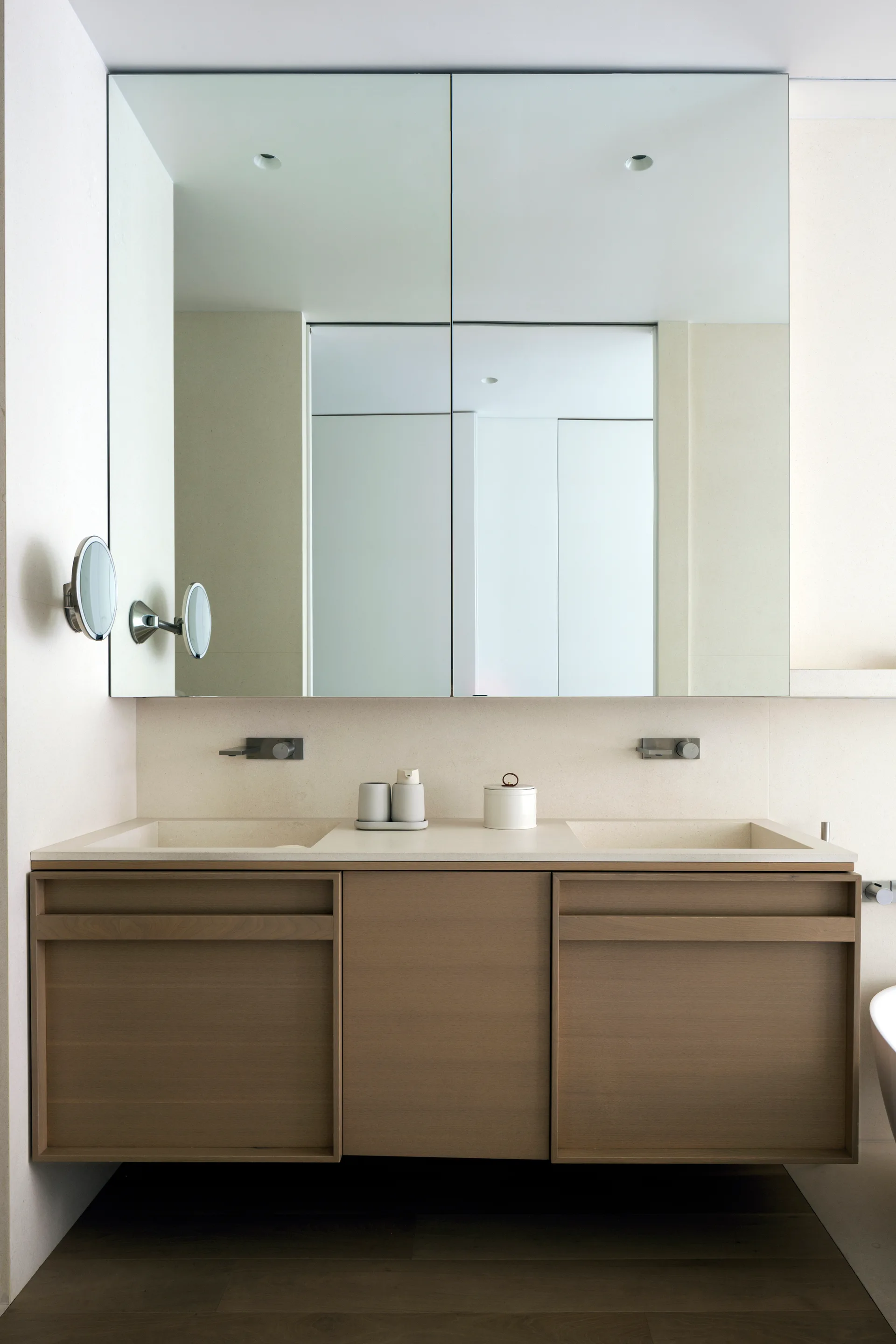 A floating light wood double vanity with integrated stone sinks is paired with a large rectangular mirror and wall-mounted faucets.