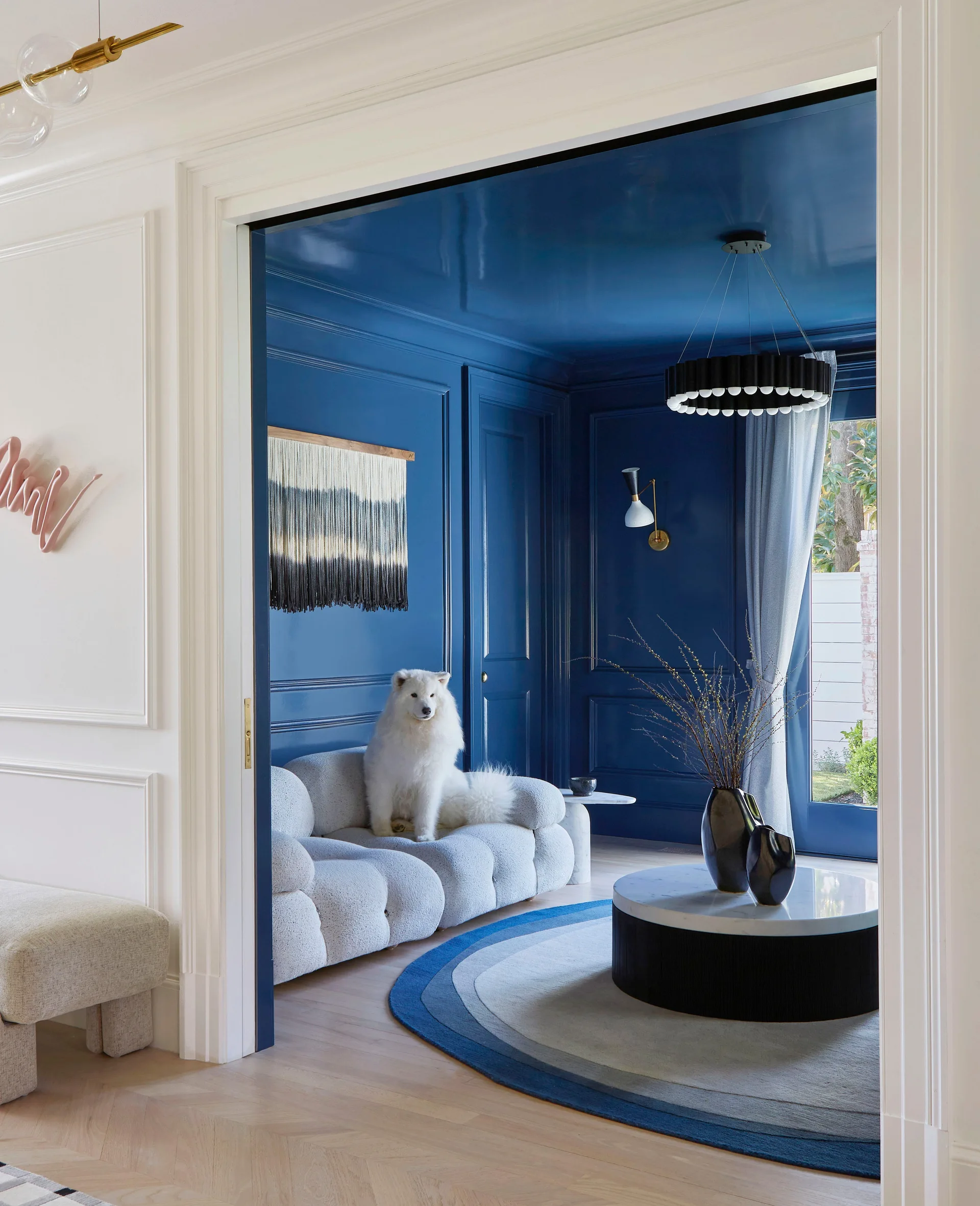 A view through a white doorway into a deep blue lacquered living room featuring a white modular sofa, a circular marble coffee table, and a blue rug.