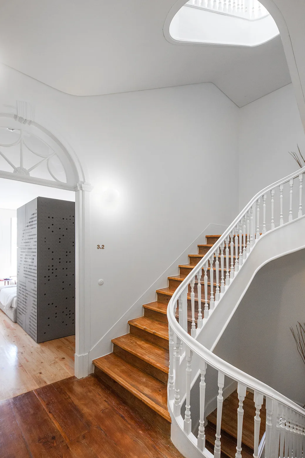 A curved white staircase with warm wood treads stands next to a classic arched entryway.