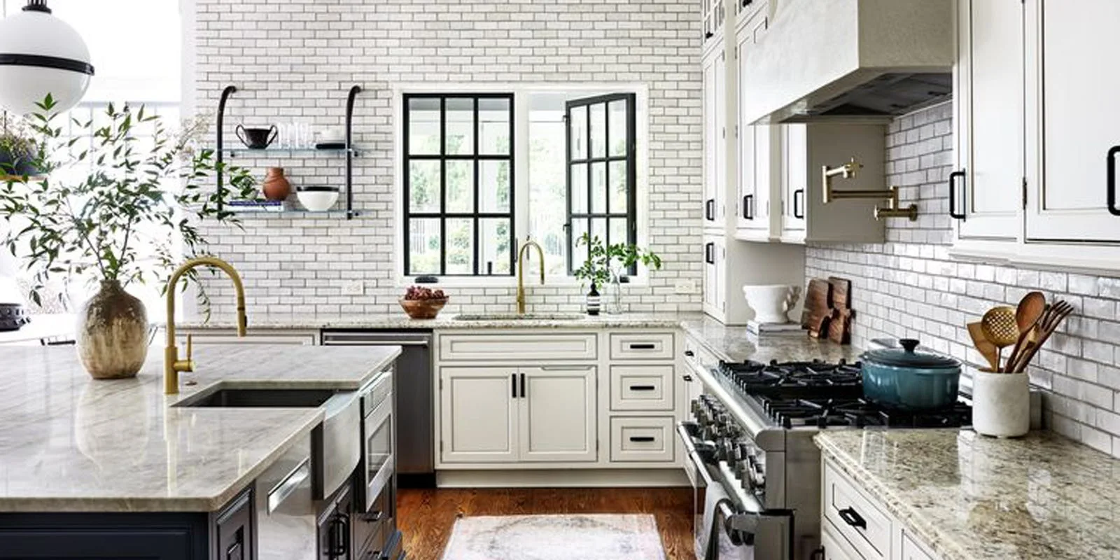 A transitional kitchen features white cabinets, a subway tile backsplash wall, black-framed windows, and an island with a brass faucet.