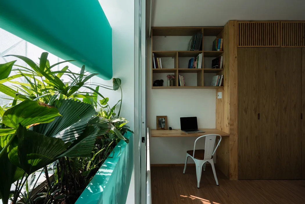 A minimalist home office features a floating wooden desk, built-in shelving, and a bright teal indoor planter filled with leafy green plants.