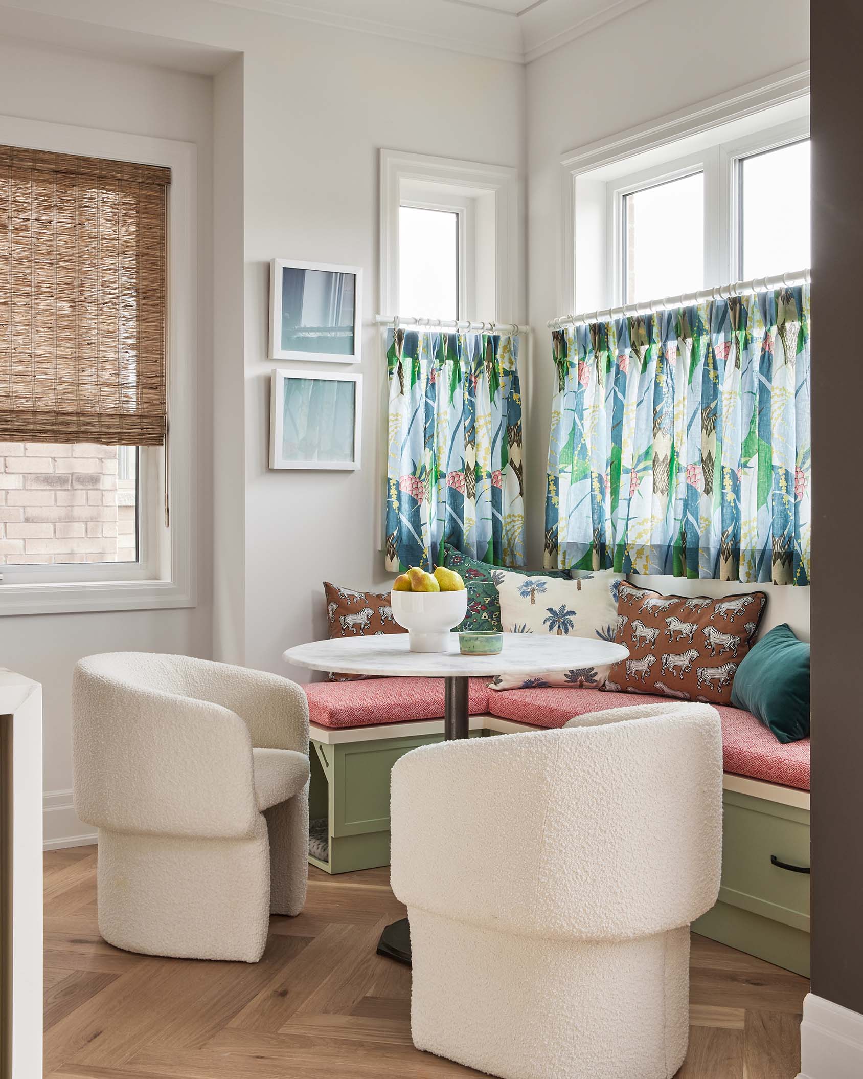 A breakfast nook features a green corner banquette, a marble-topped pedestal table, and two textured cream boucle chairs on wood flooring.