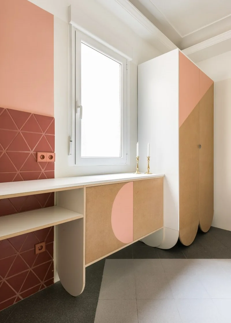 Custom peach and wood-toned cabinetry with scalloped bases stands next to a window and a terracotta geometric tiled wall desk area.