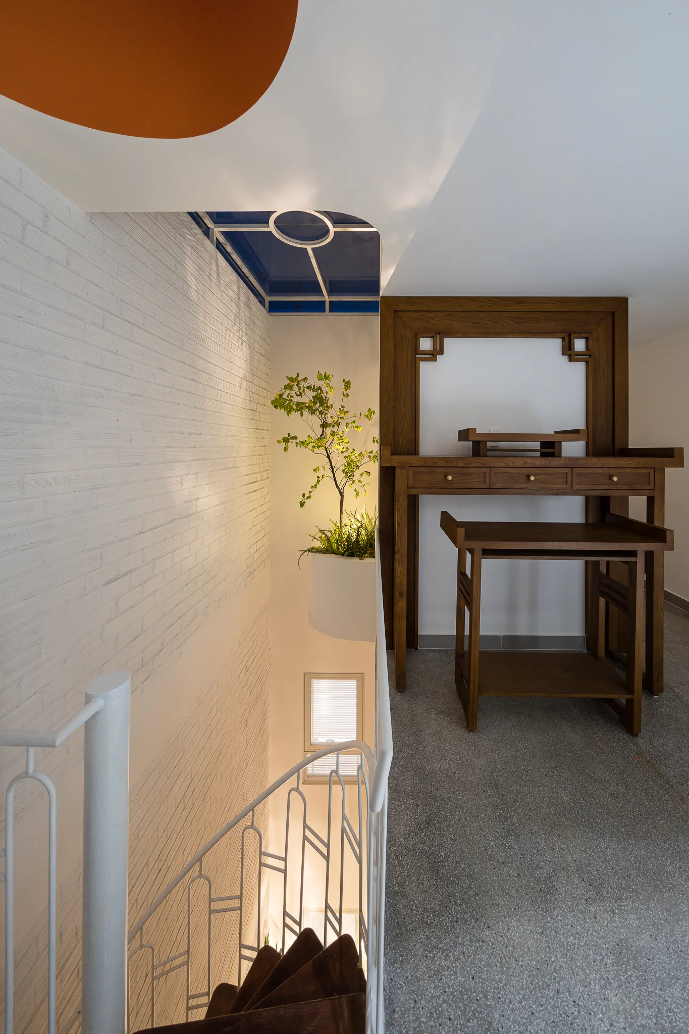 A modern staircase landing with a dark wood console table, a white metal railing, and a painted white brick wall.