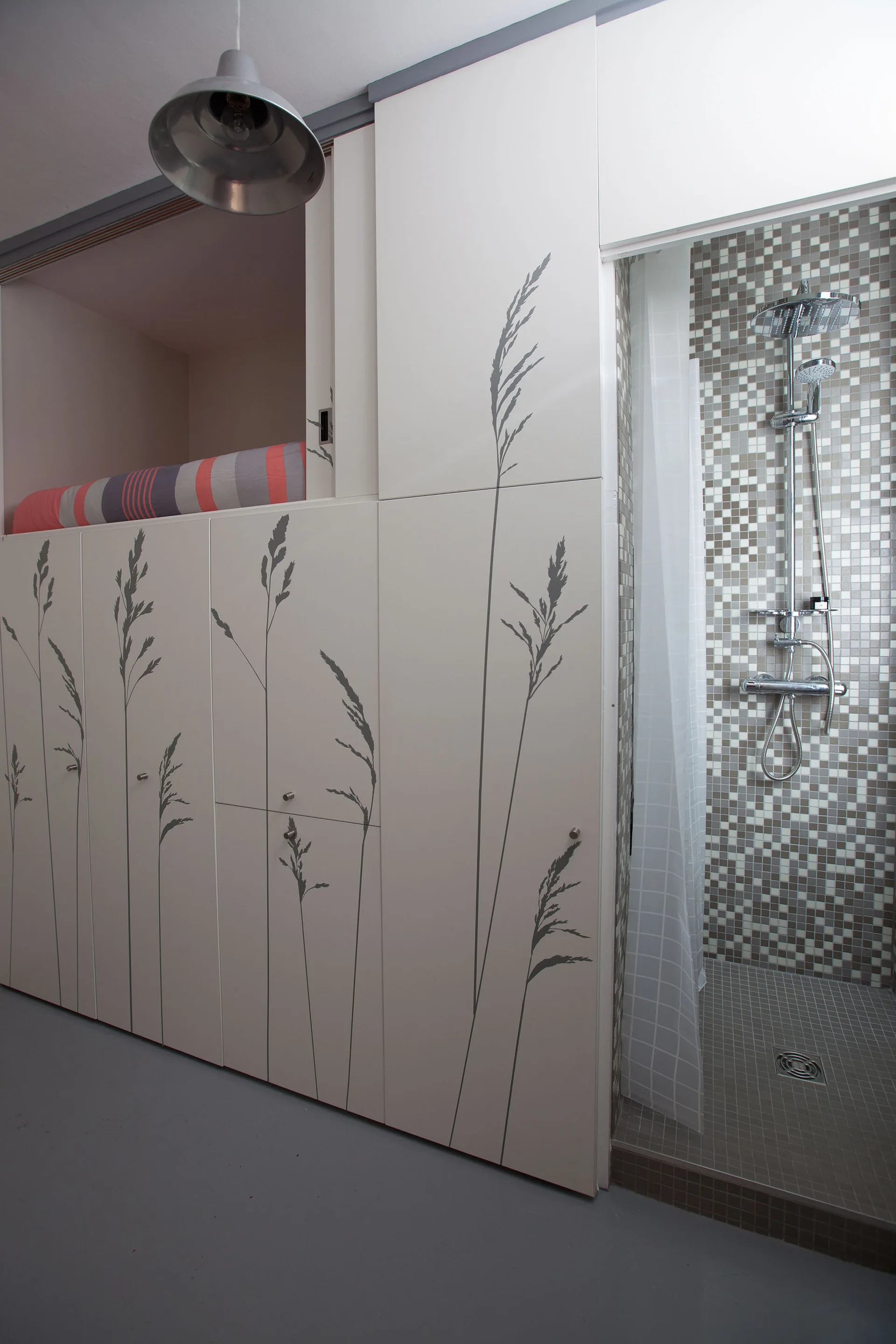 A modern bathroom features floor-to-ceiling white cabinetry printed with grey grass stems next to a walk-in shower with mosaic tiles.