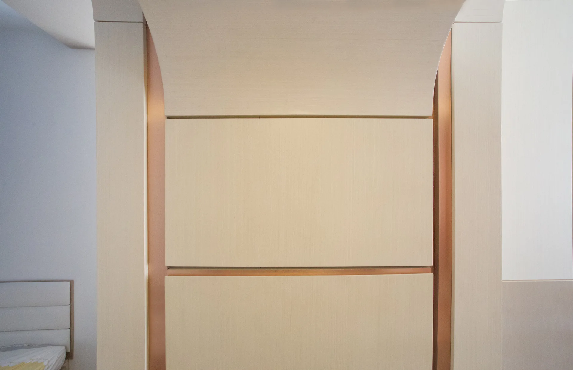 A close-up of bedroom wall paneling made of light tan wood panels divided by vertical copper metal trim.