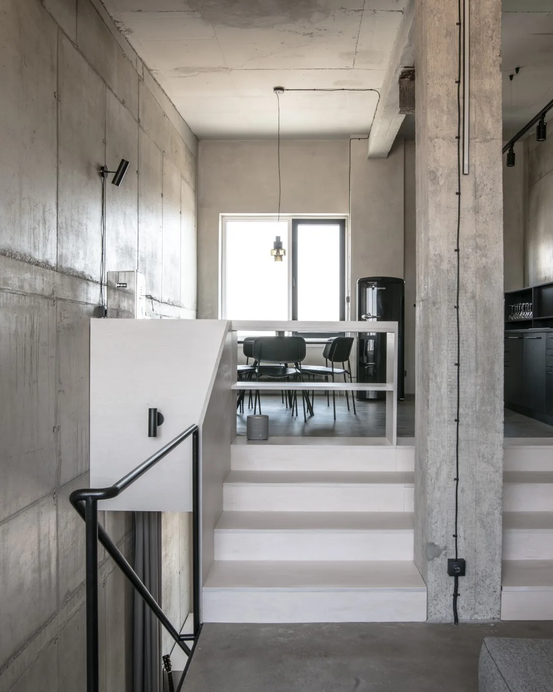 A light plywood staircase with a black metal handrail is built against a raw concrete wall in an industrial loft apartment.