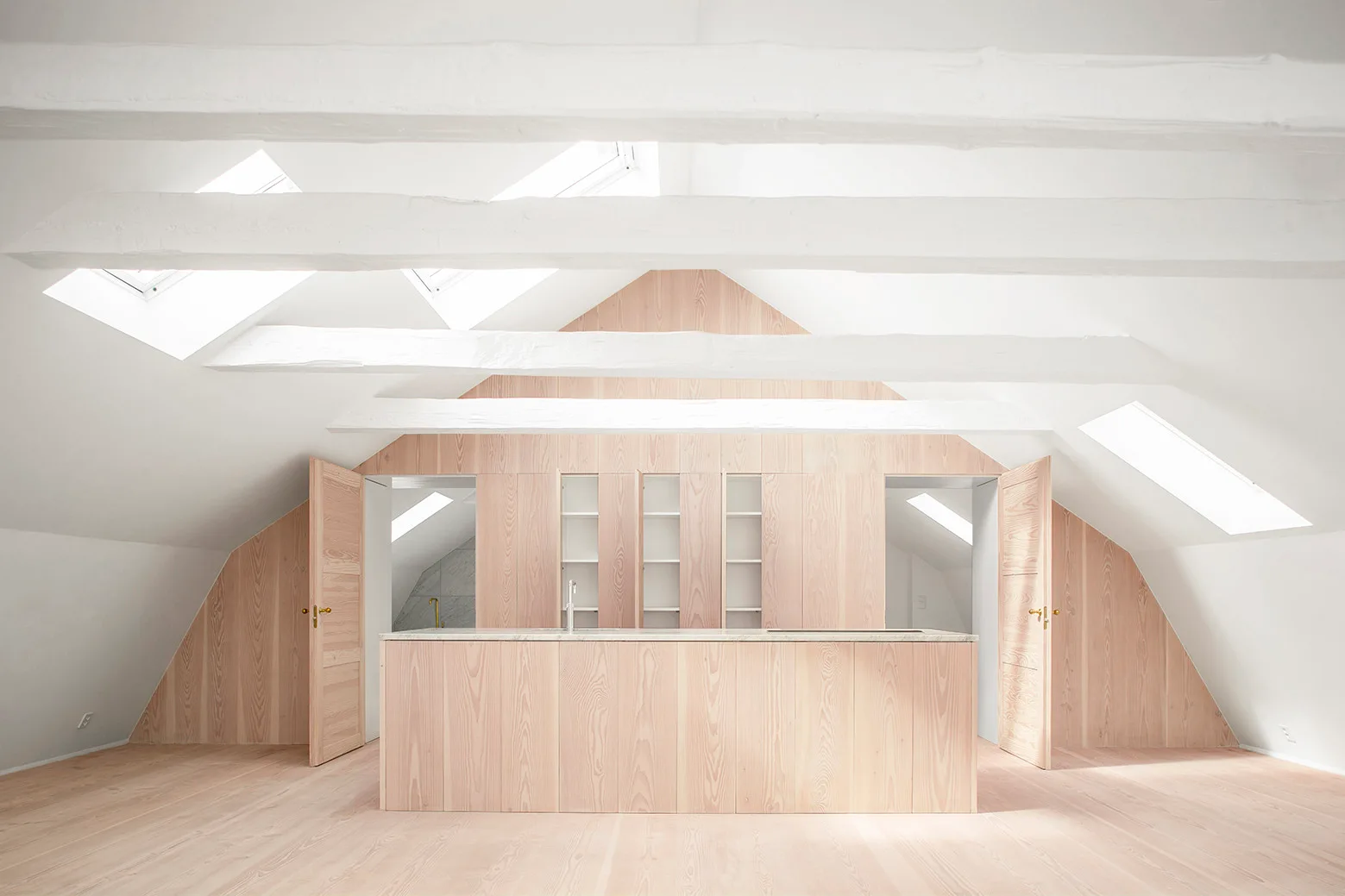 Minimalist attic kitchen featuring a light wood island and paneled cabinetry under white sloped ceilings with skylights and exposed beams.