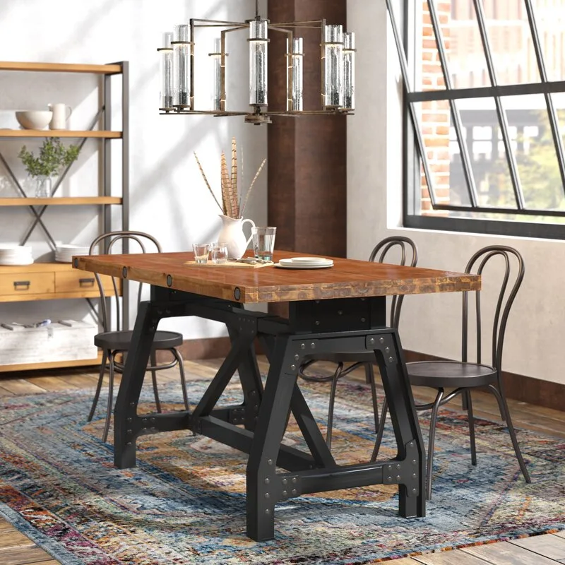 An industrial dining room with a wood-topped dining table on black metal legs, surrounding chairs, and a colorful patterned area rug.