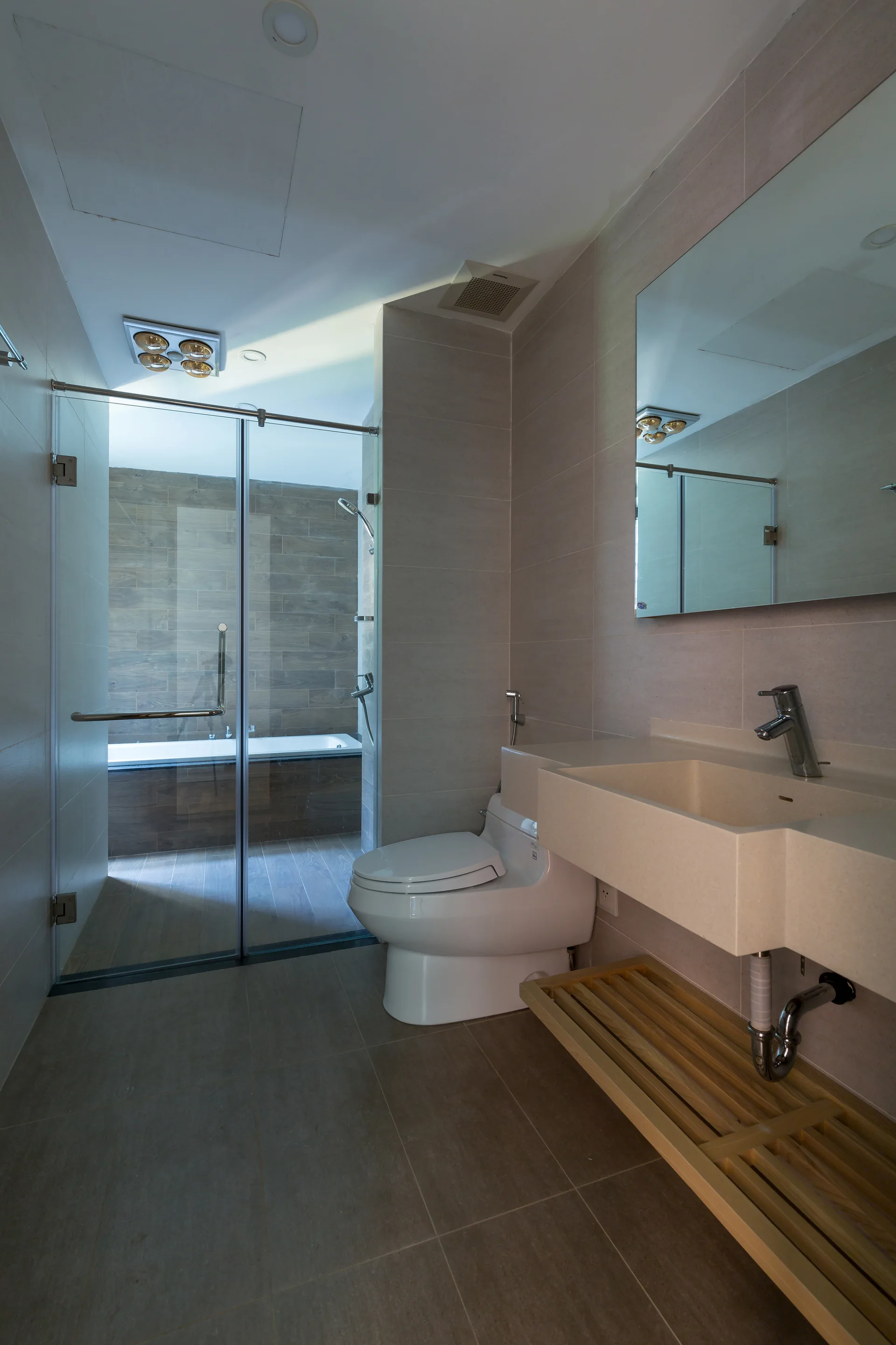 A modern bathroom features a grey tiled floor, a wall-mounted stone sink with a wooden slatted shelf beneath, and a glass-enclosed shower.