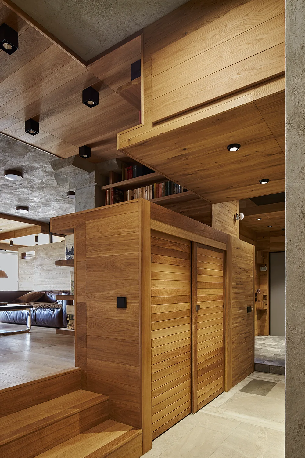 A split-level interior features warm wood wall panels, a slatted sliding door closet, wooden stairs, and a concrete ceiling with recessed lights.