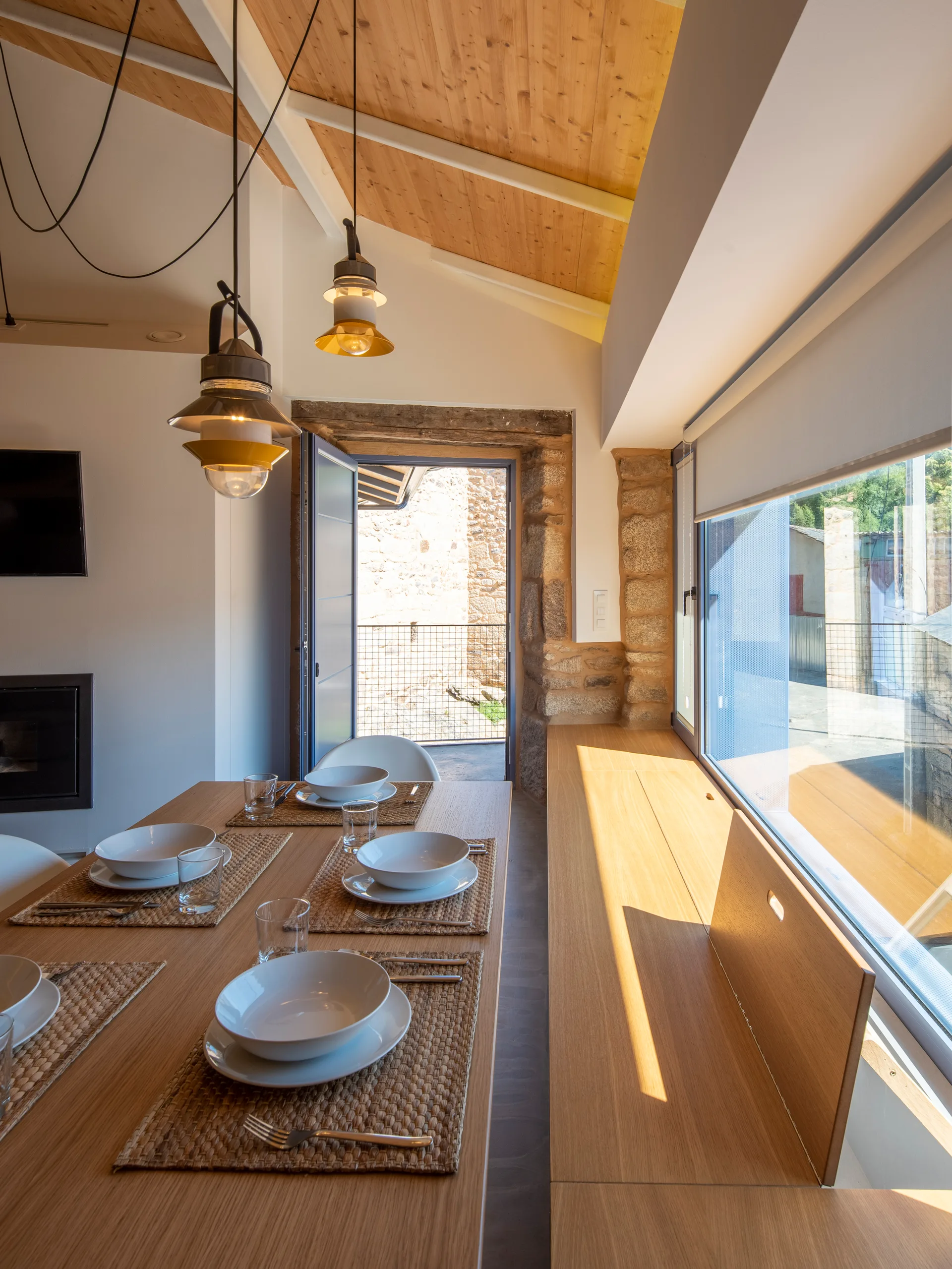 A wooden dining table with place settings sits next to a built-in bench under a sloped wood ceiling.