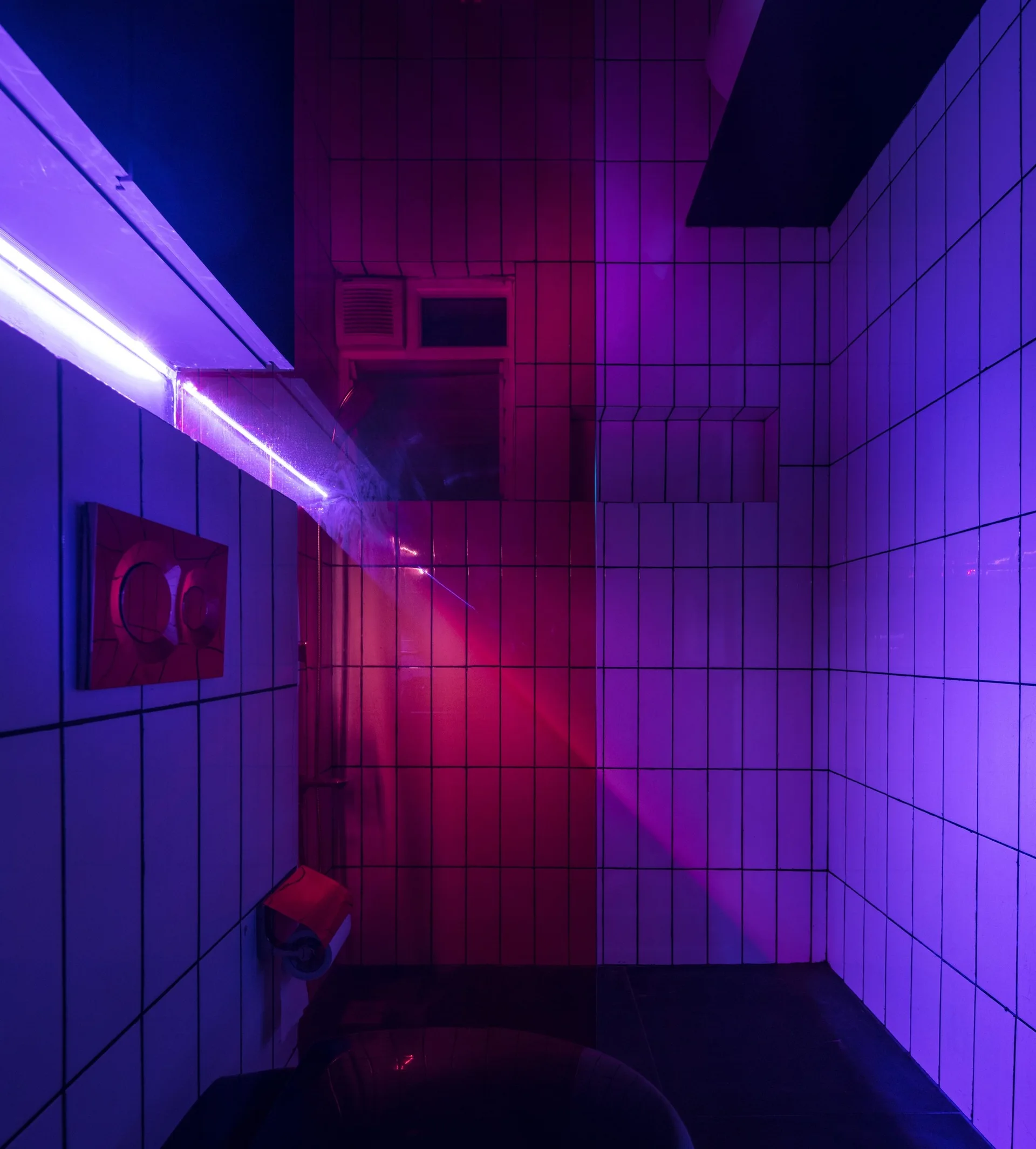 A bathroom with white square-grid wall tiles is dramatically illuminated by vibrant purple and magenta neon accent lights.