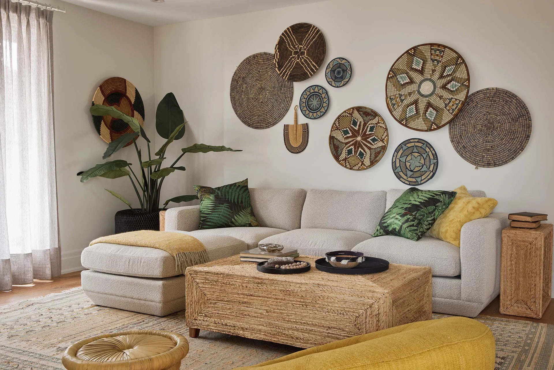 An off-white sectional sofa sits behind a woven coffee table, accented by a curated collection of patterned woven baskets on the wall.