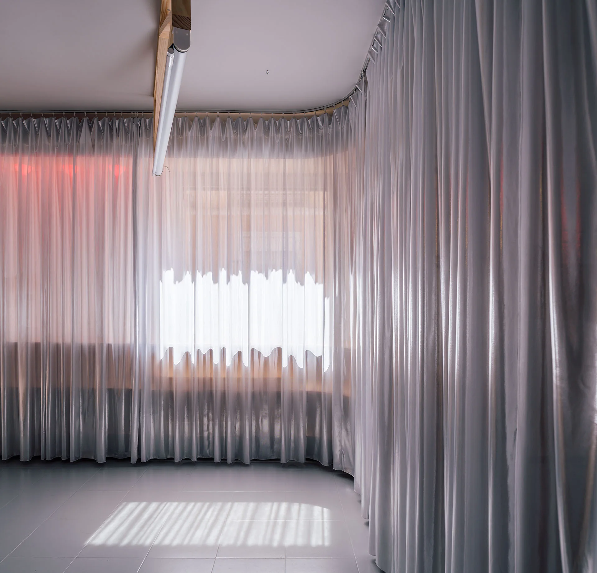A modern interior featuring a curved ceiling track with floor-to-ceiling sheer curtains and light tiled flooring.
