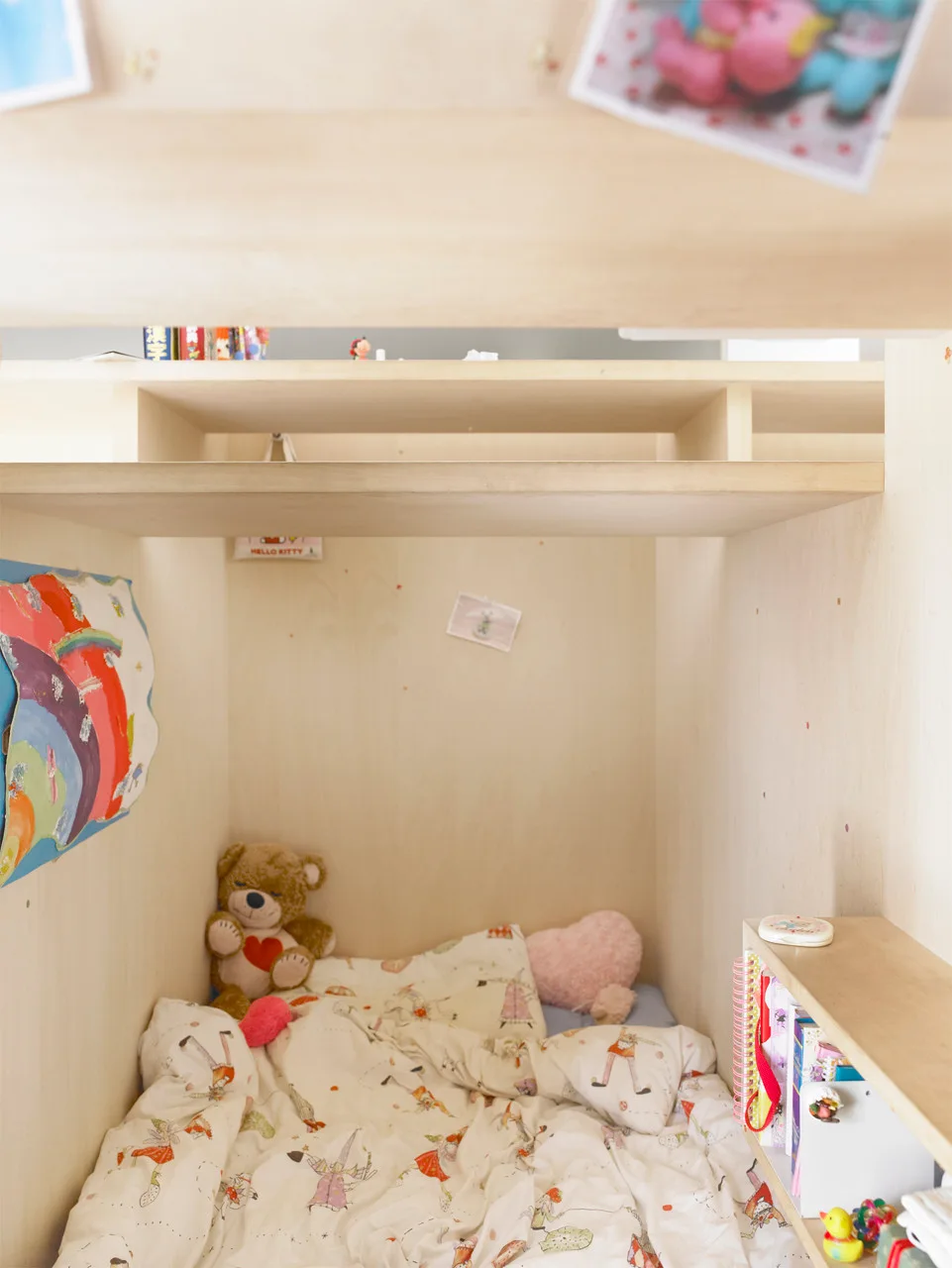 A cozy child's sleeping nook crafted from light plywood features integrated shelving, whimsical bedding, and soft stuffed animals.