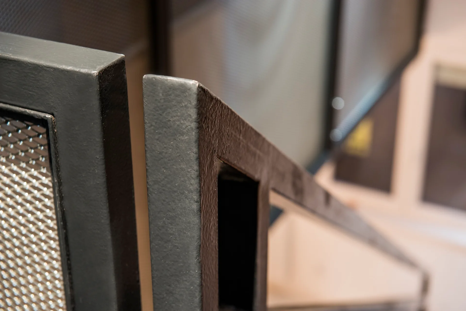 A close-up of a matte black metal staircase railing with a textured frame and an integrated wire mesh panel.