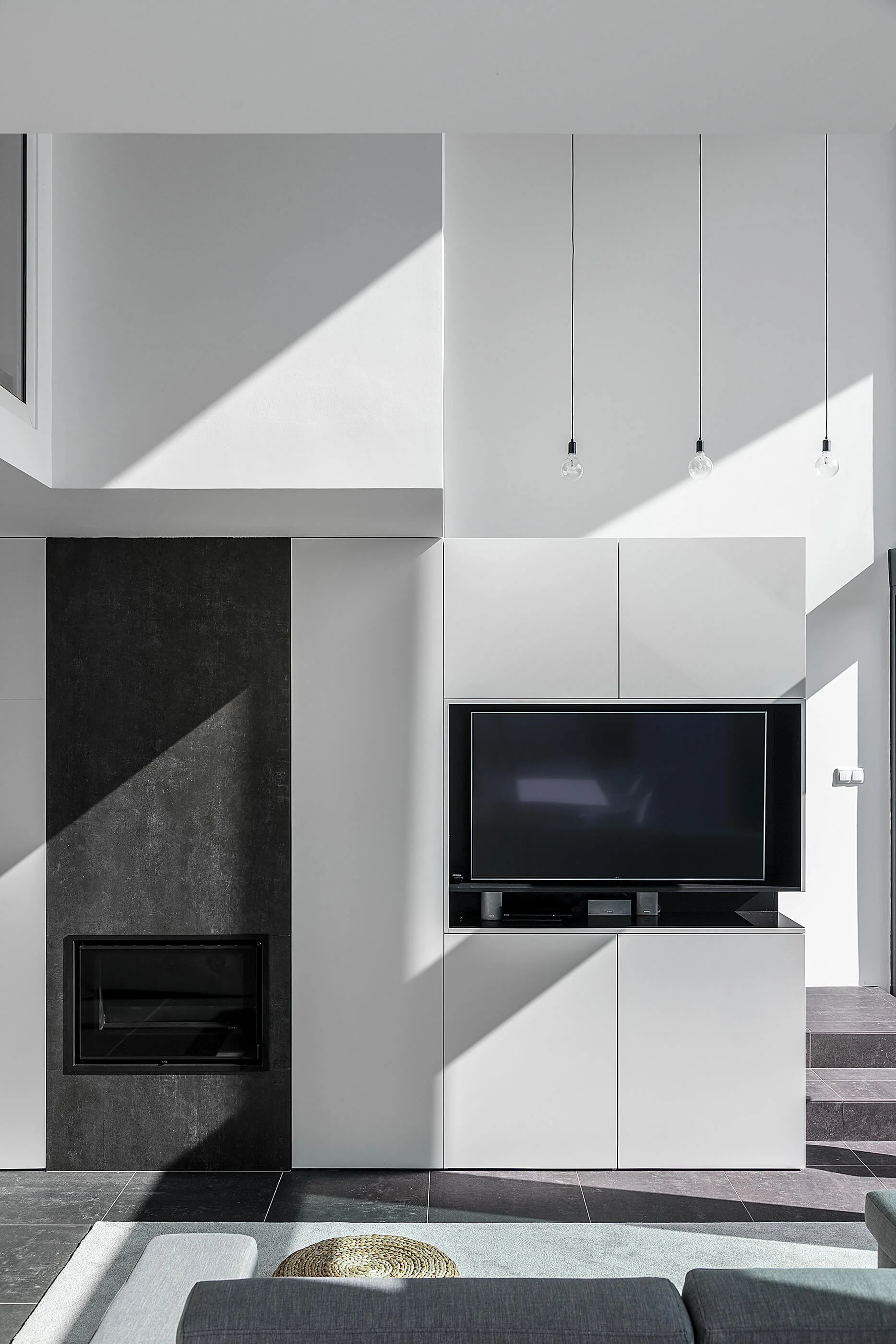 A minimalist living room features a vertical black fireplace column next to a white built-in media cabinet with an integrated television.