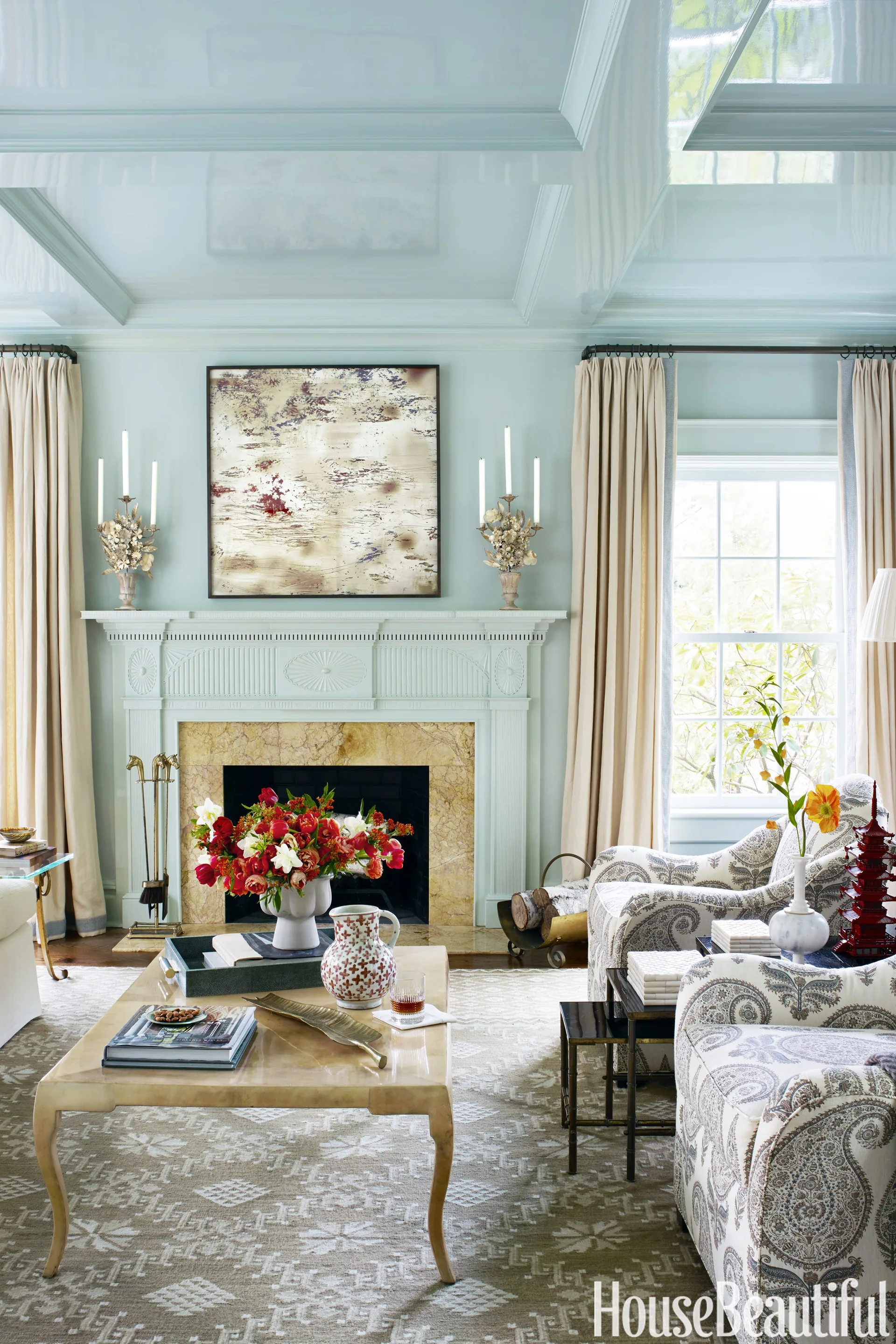 A light blue living room features a high-gloss lacquered ceiling, a classic fireplace with a marble surround, and paisley patterned armchairs.