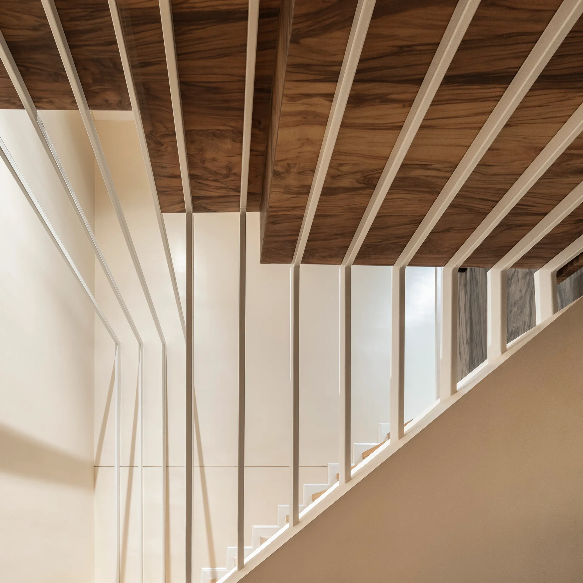 A close-up of modern stairs with walnut wood treads and slim, vertical off-white metal balusters against a neutral wall.