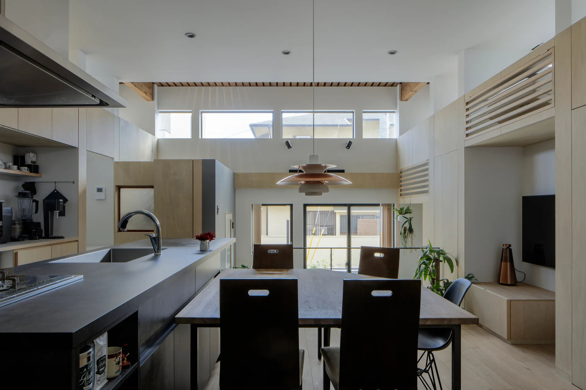A modern open dining and kitchen space with a wood dining table, dark kitchen island, and light wood wall cabinetry under transom windows.
