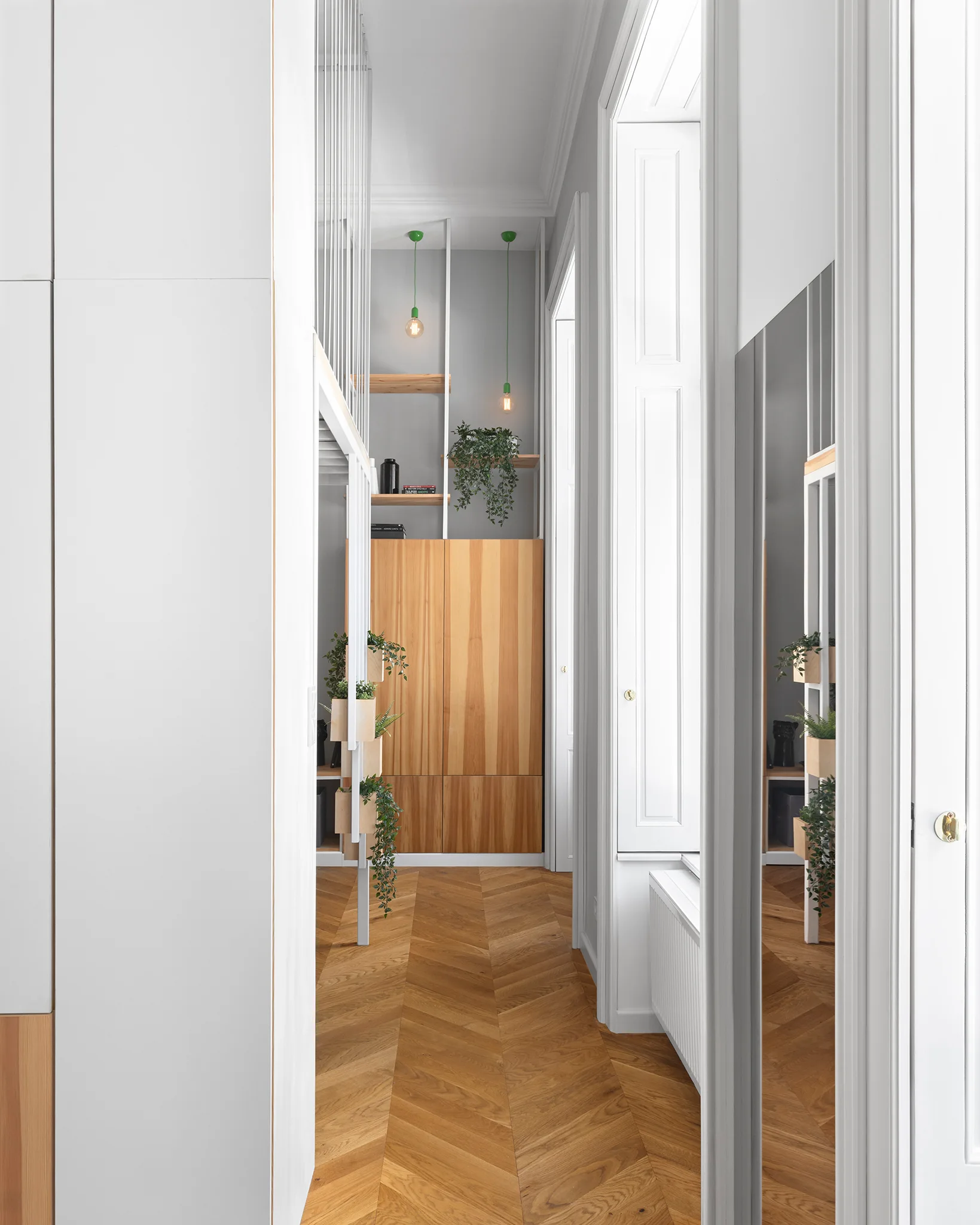 A bright hallway features light-toned herringbone wood flooring, custom built-in wood cabinetry with open shelving, and hanging green pendant lights.