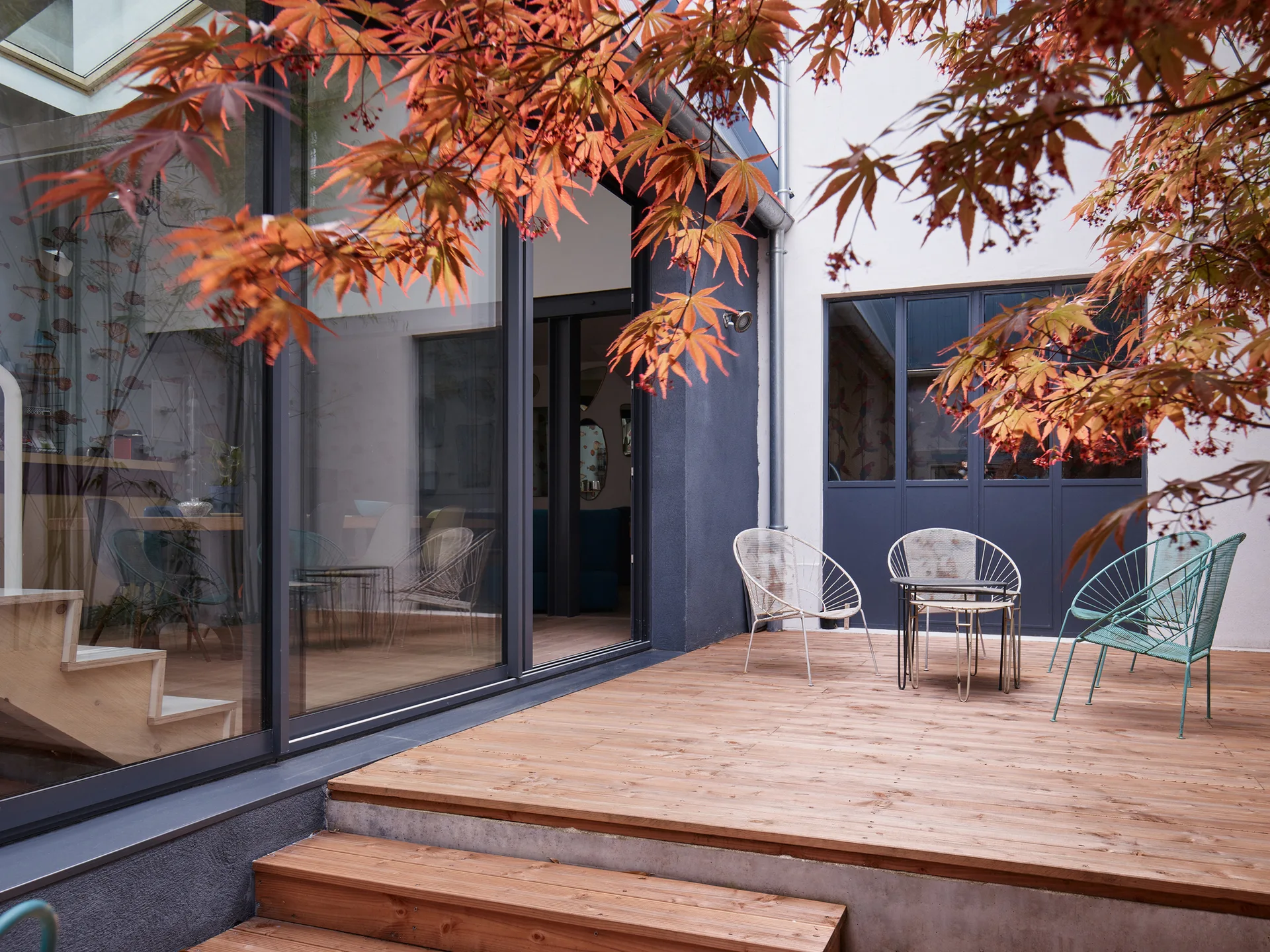 A wooden patio deck with metal wire chairs and small nested tables next to sliding glass doors.