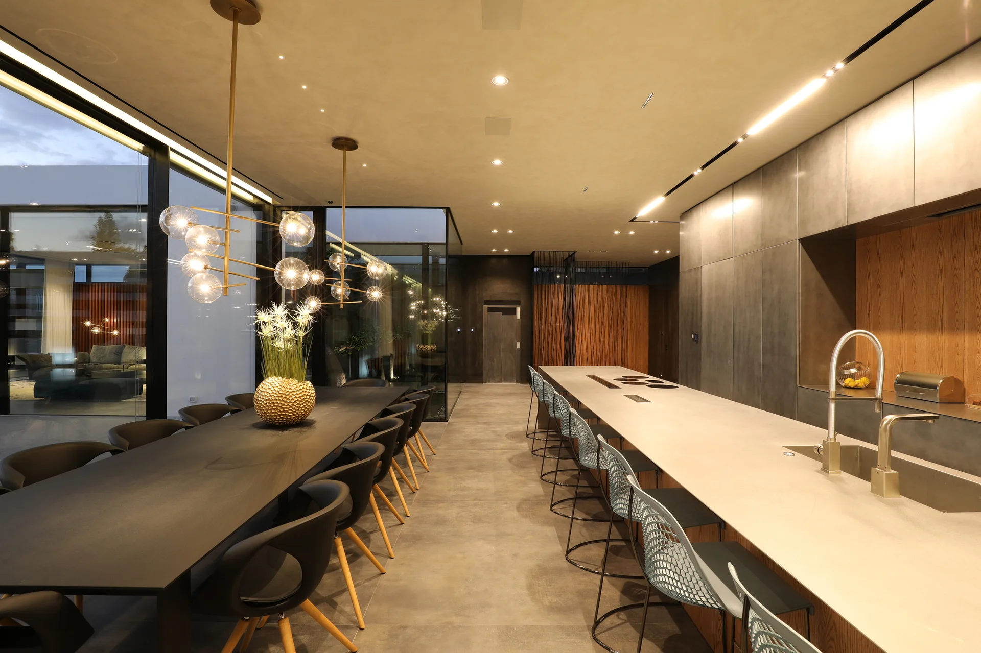 A spacious open-concept kitchen and dining room featuring a long black dining table, a massive grey island with mesh barstools, and gold globe pendant lights.
