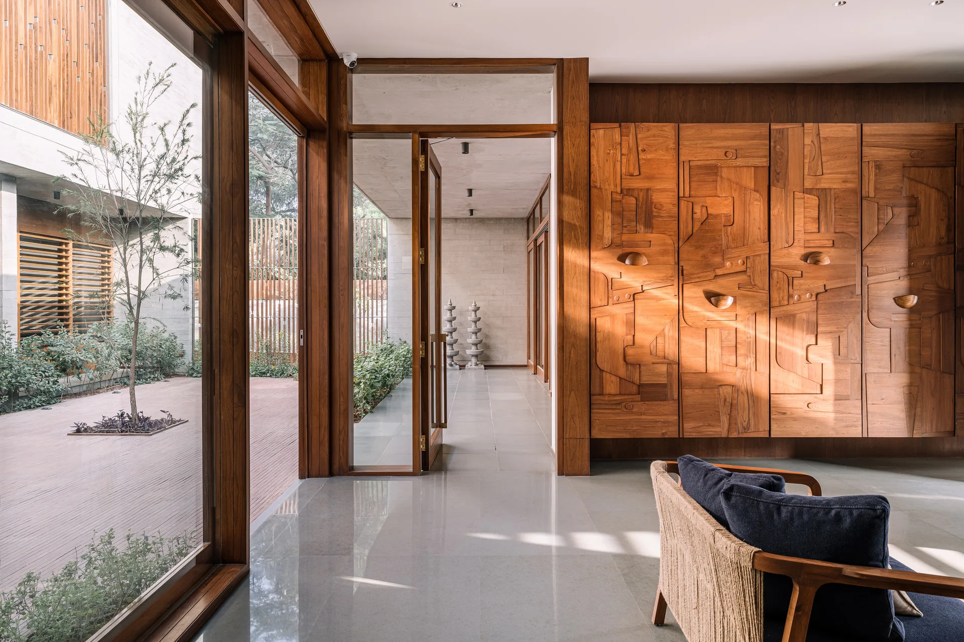 A modern entryway features a large carved wood cabinet wall, polished stone floors, and glass doors opening to an outdoor courtyard.