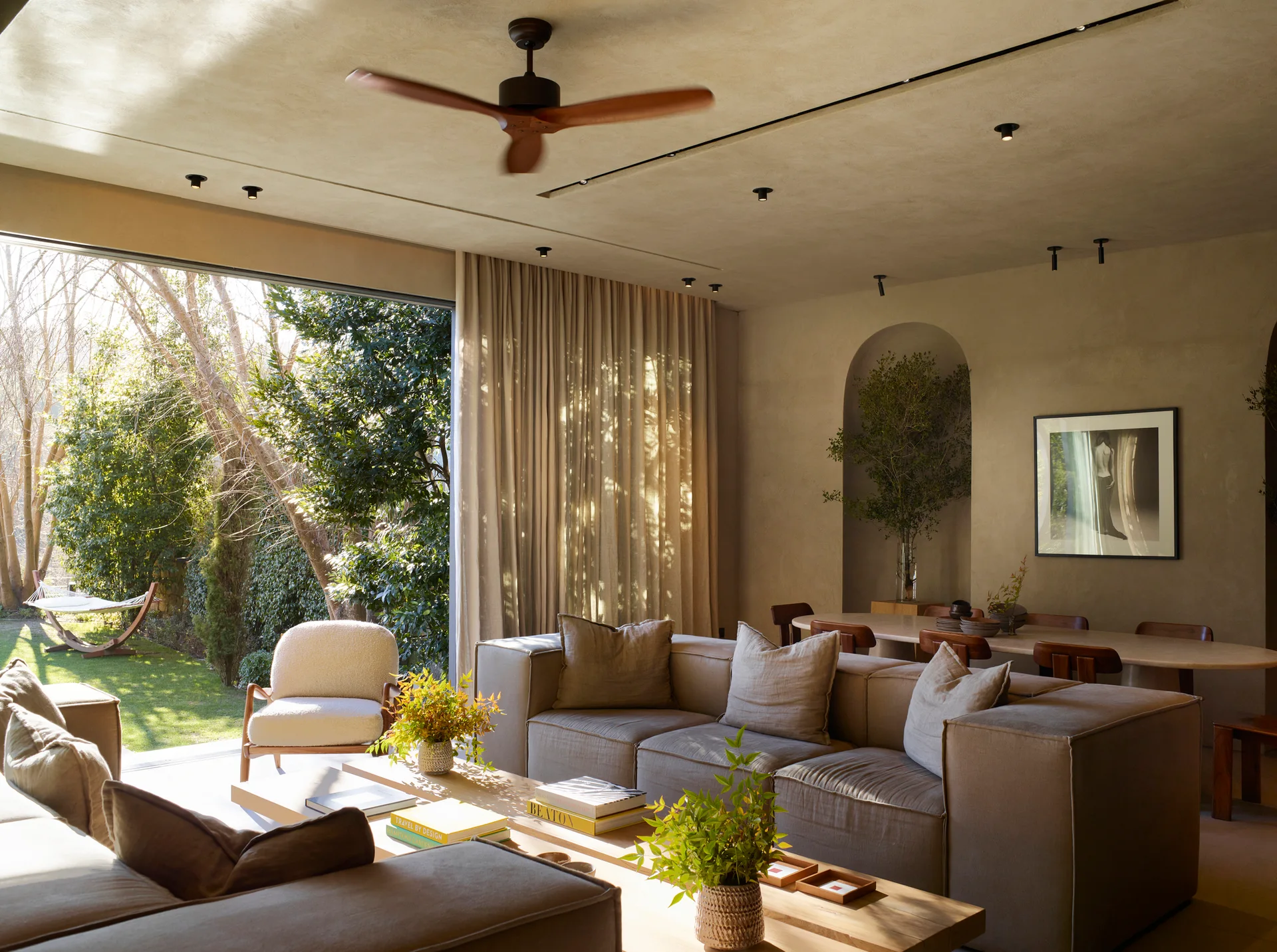 A neutral modern living room featuring plaster walls, a taupe modular sofa, and large sliding glass doors that open to a green garden.