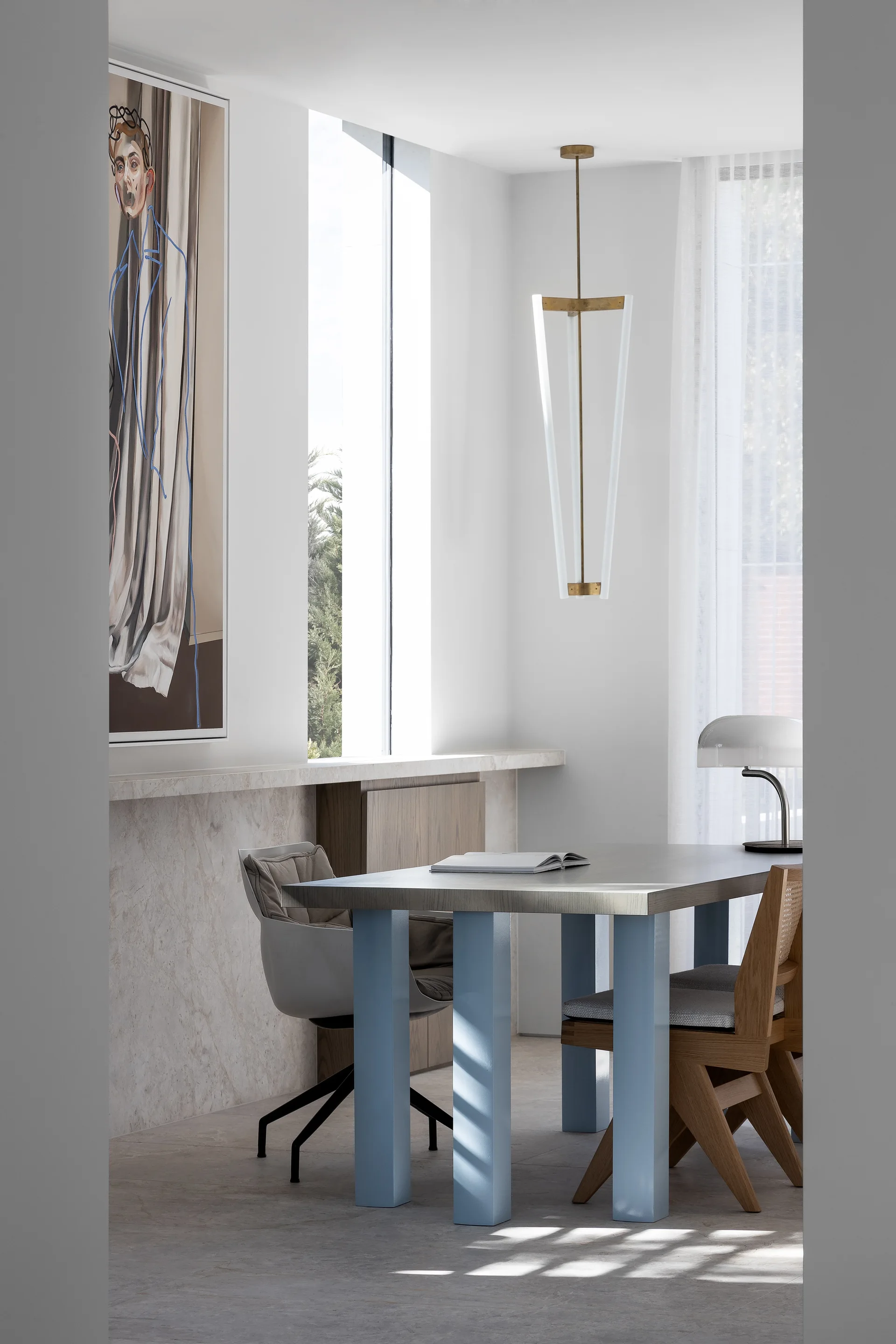 A contemporary dining room features a wood-top table with light blue legs, a low stone wall ledge, and a large abstract painting.
