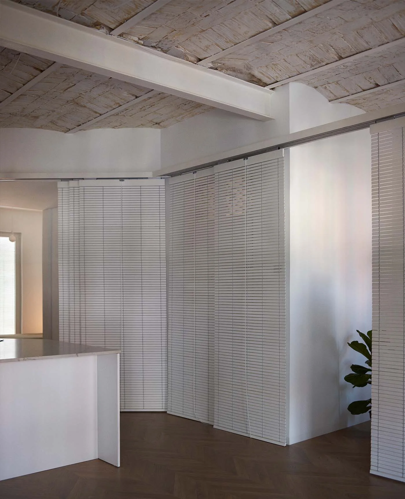 White sliding slatted blinds serve as a room partition beneath an exposed painted brick vaulted ceiling and herringbone wood floors.