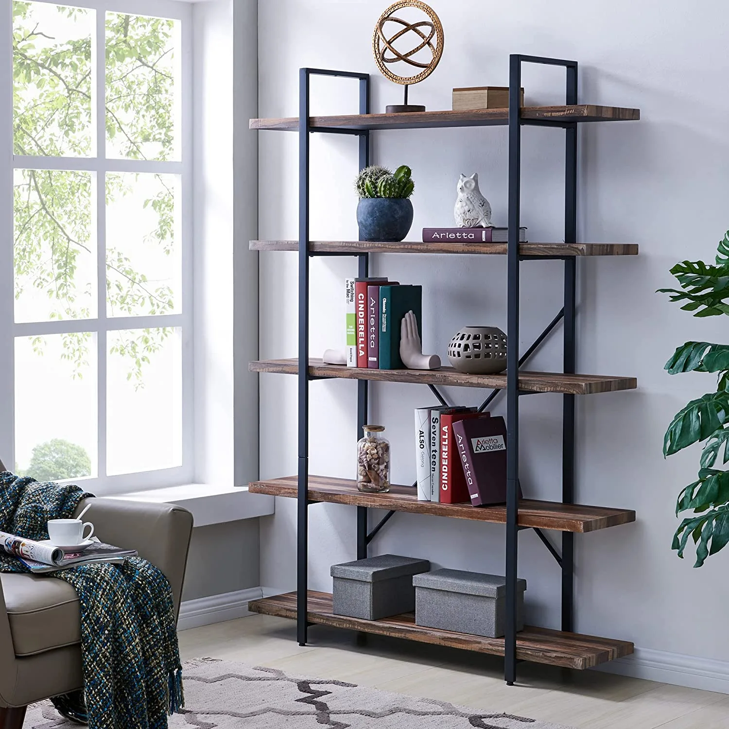 An industrial-style bookshelf with five wood-toned shelves and a black metal frame stands against a white wall next to a bright window.