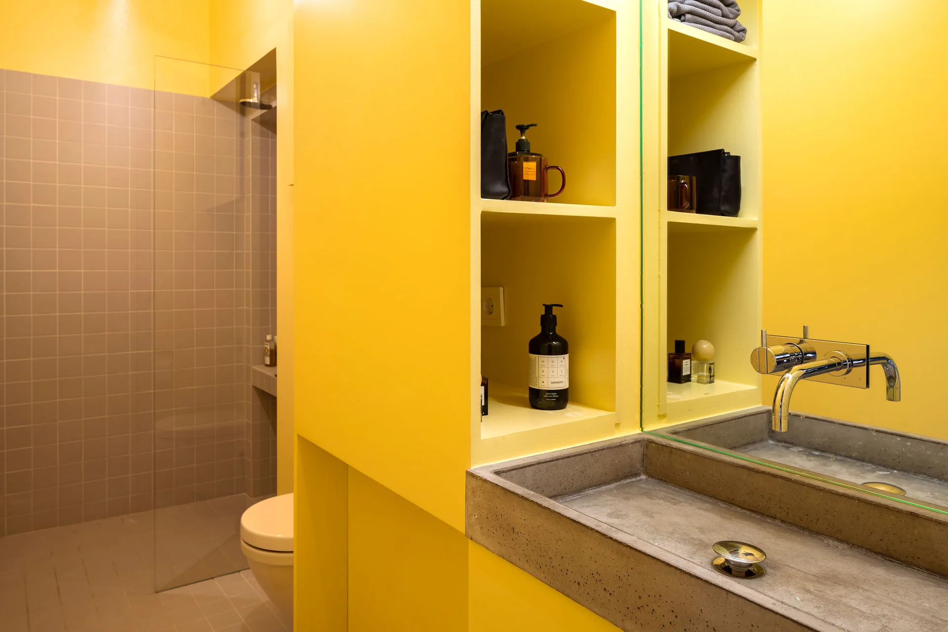 A modern yellow bathroom vanity featuring a matte concrete sink basin, integrated open shelves, and a wall-mounted faucet.