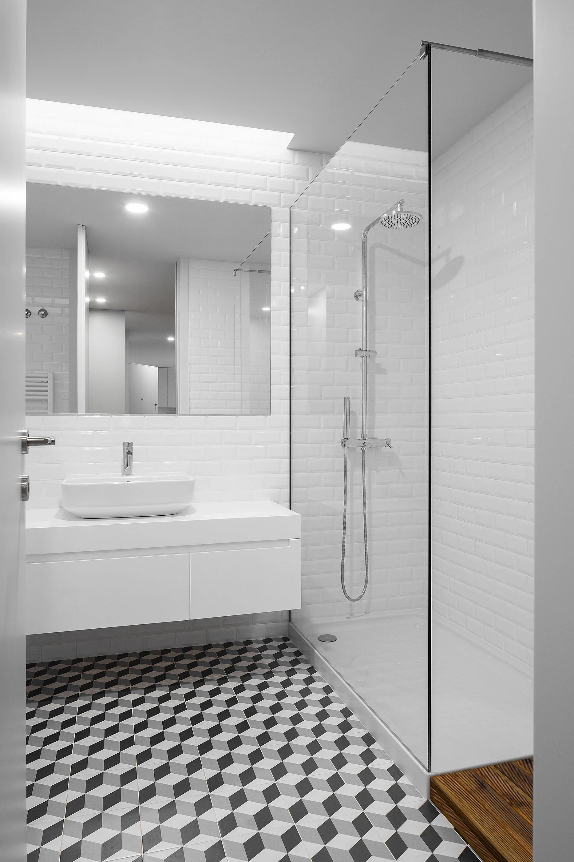 A minimalist bathroom features white subway tile walls, a floating vanity with a vessel sink, and black and white geometric floor tiles.